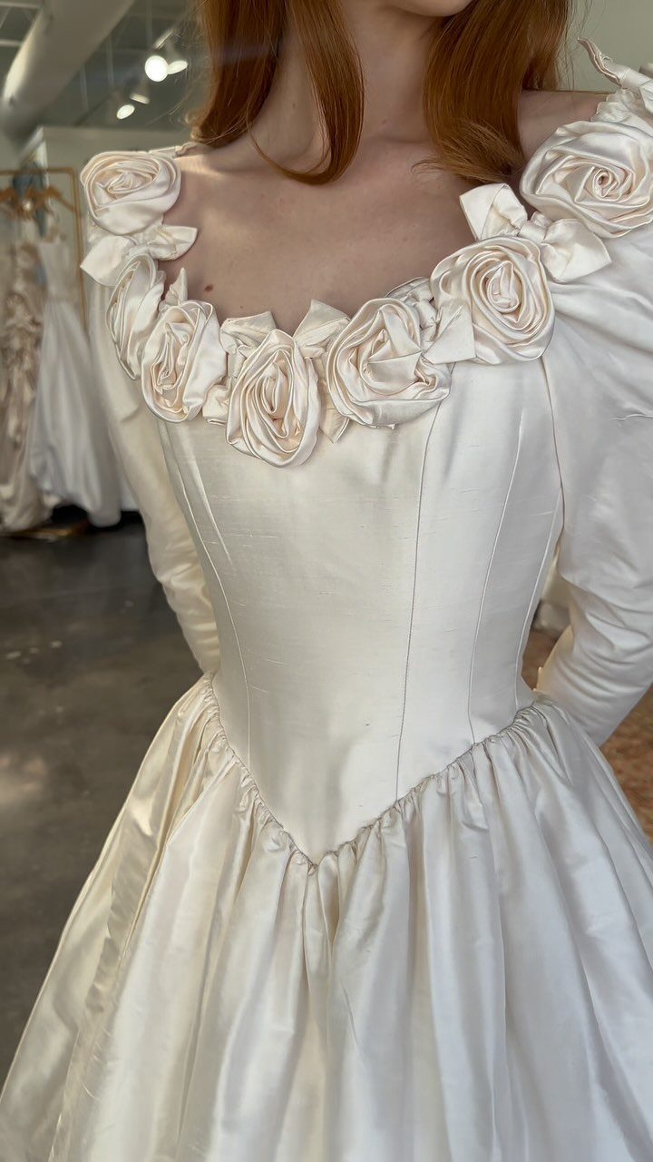 1989 Wedding Dresses: 8 Details That Defined the Look 8 A woman wearing a white satin wedding dress with large fabric rose appliqués around the neckline.