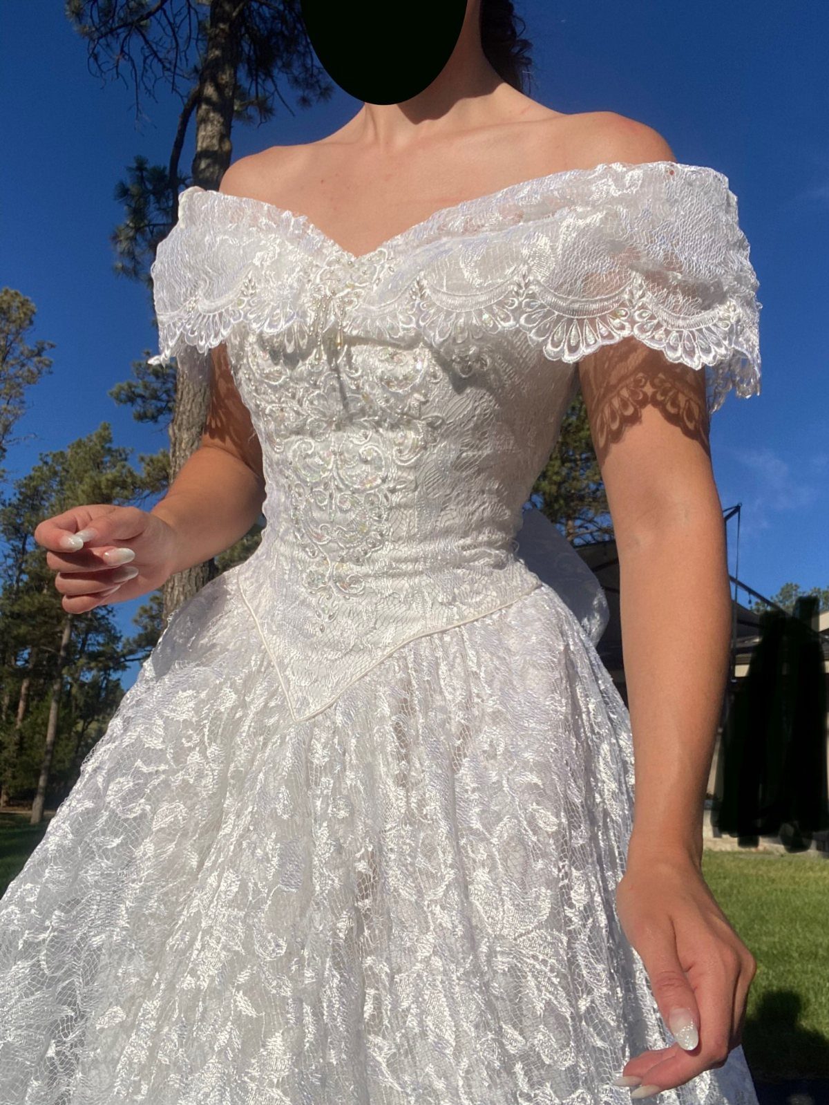 1989 Wedding Dresses: 8 Details That Defined the Look 2 A person wearing a white lace off-the-shoulder wedding dress with a voluminous skirt outdoors.