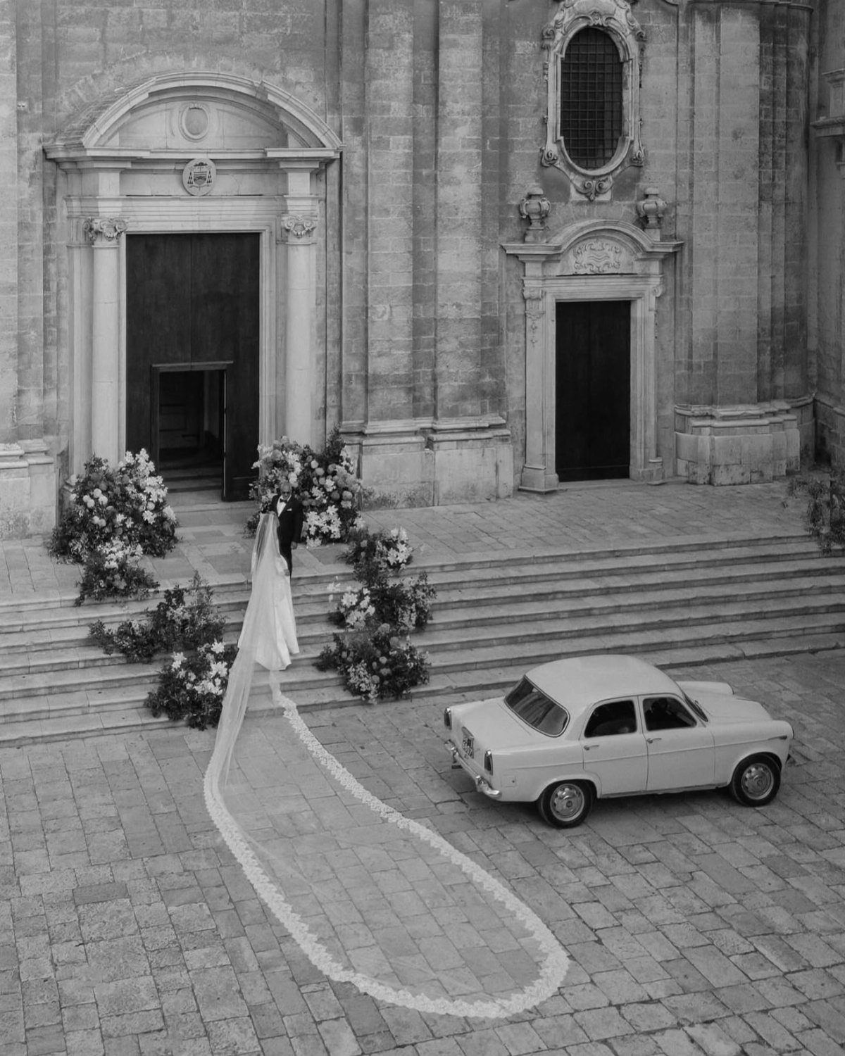 1989 Wedding Dresses: 8 Details That Defined the Look 3 A bride in a white dress with an extremely long, flowing lace-edged veil on cobblestones.