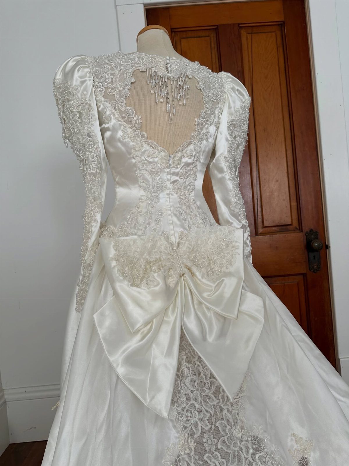 1989 Wedding Dresses: 8 Details That Defined the Look 7 A white satin wedding dress with lace sleeves and a large bow on a mannequin.