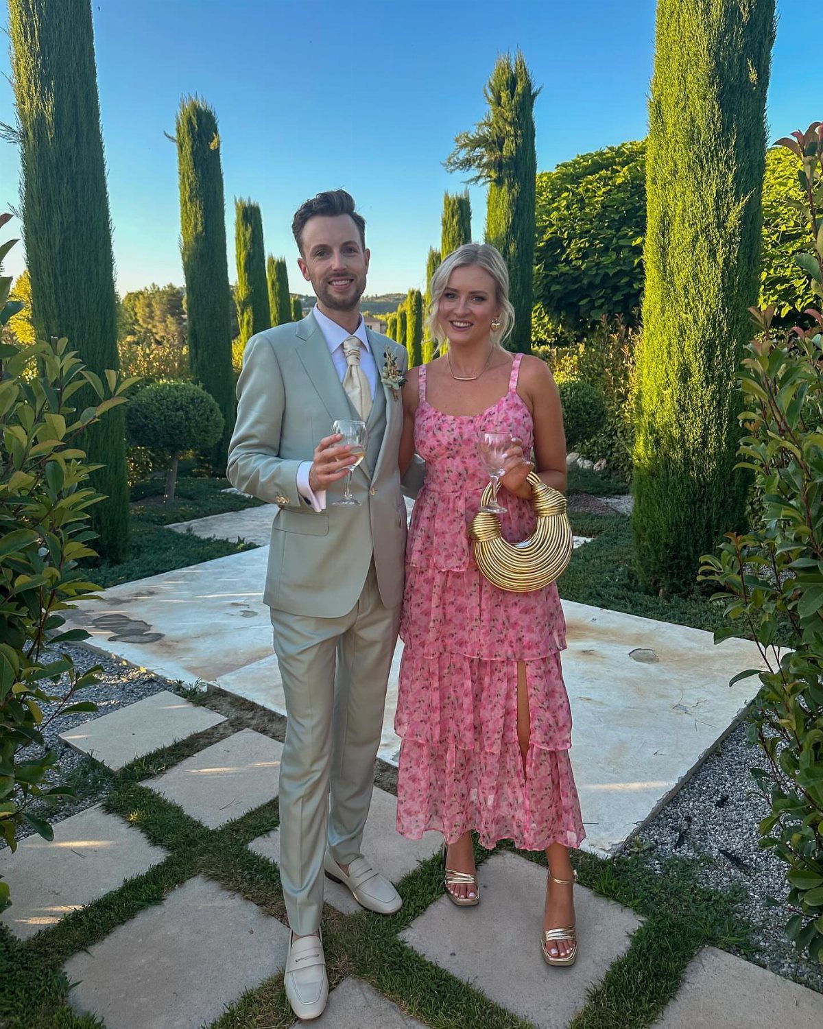 After Wedding Dress Ideas: 5 Looks Beyond the Ceremony 2 A man in a grey suit and a woman in a pink floral dress posing in a garden.
