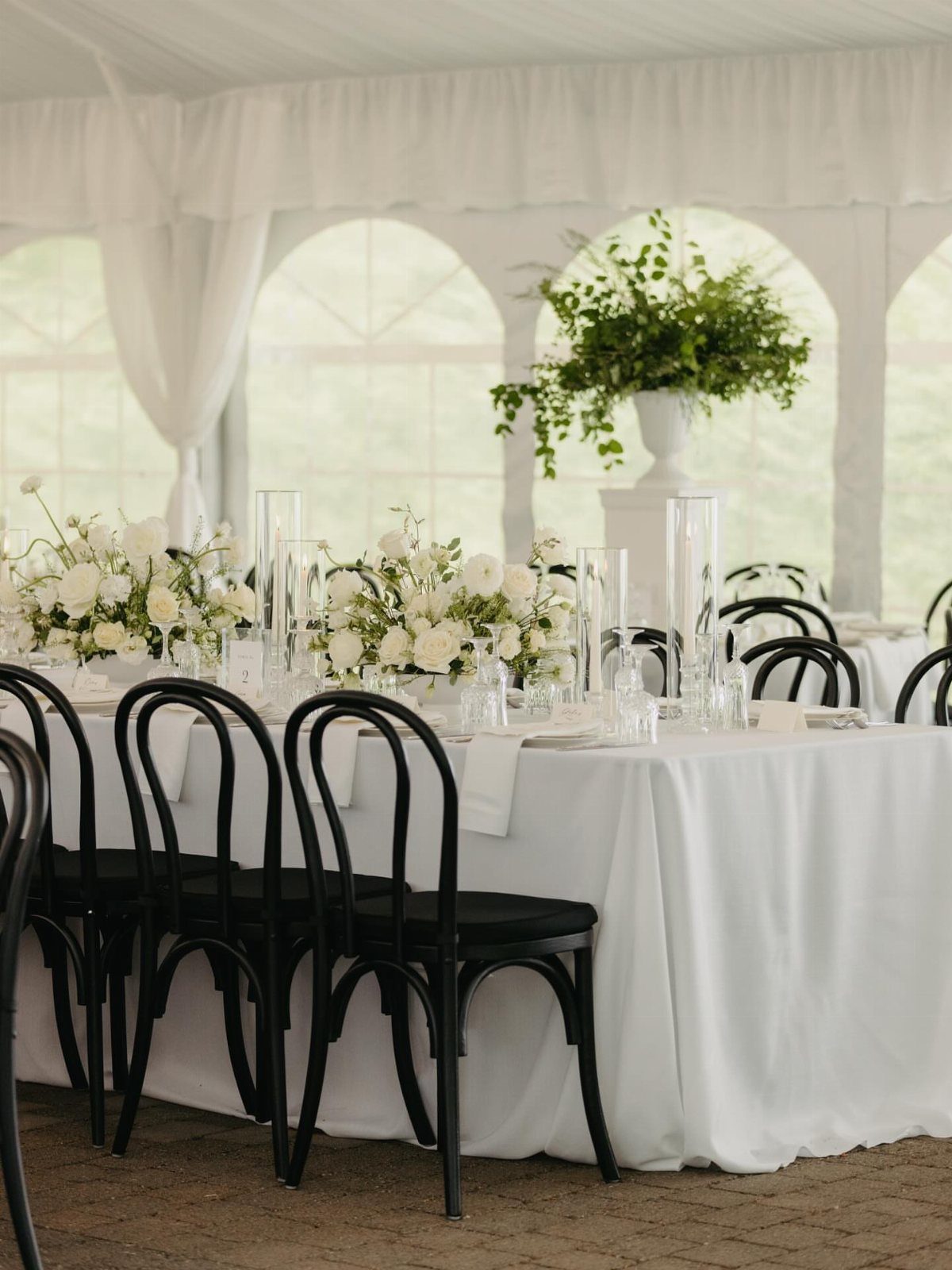 Black bentwood chairs lined up against a long table with white linens and floral arrangements.