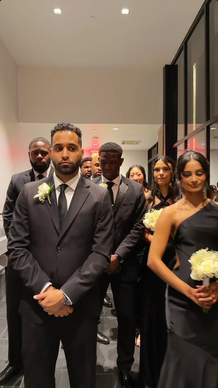 Men in black suits and black ties standing with women in black formal dresses.