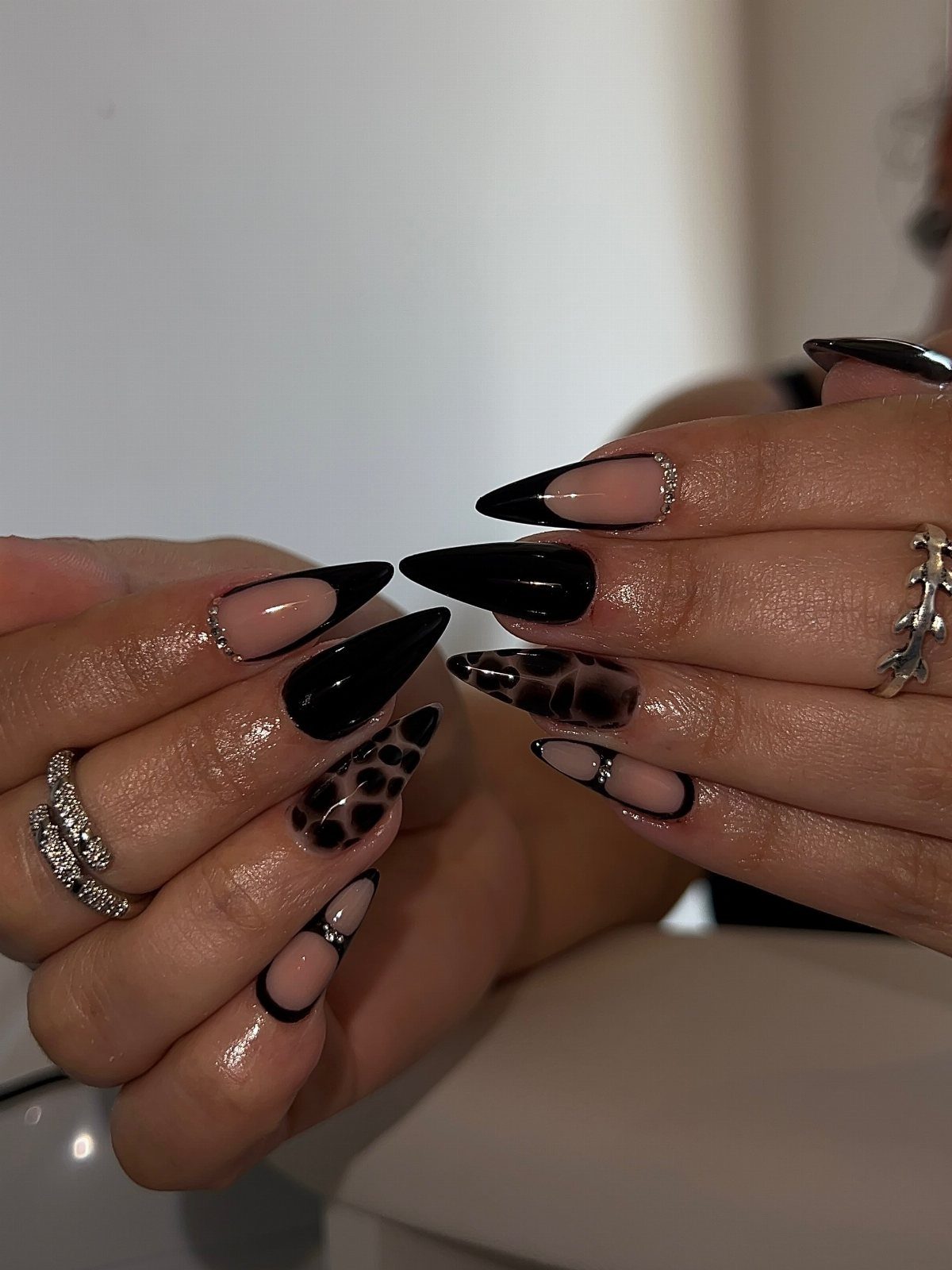 Hands displaying long almond-shaped manicured nails with black, leopard print, and silver accented designs.