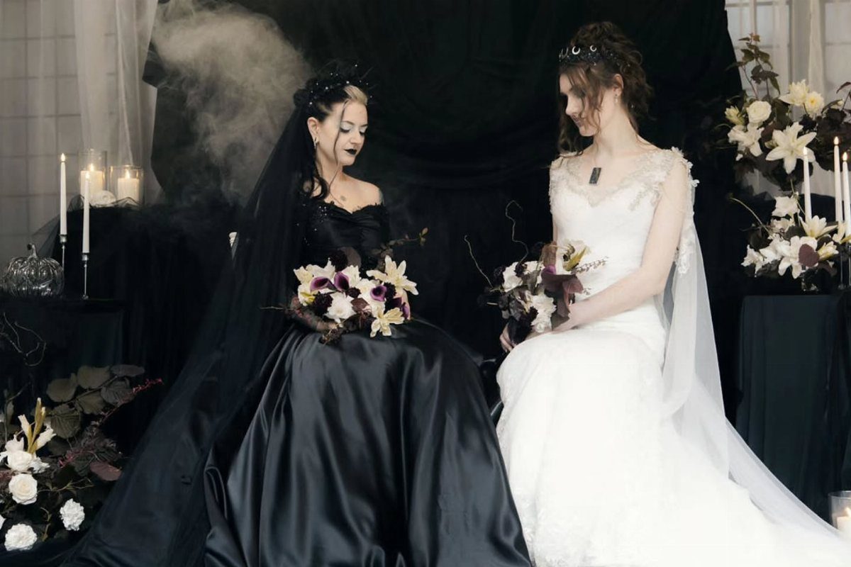8 Alternative Wedding Dresses for Every Kind of Modern Bride 7 Two women in contrasting black and white wedding dresses sitting together with floral bouquets.