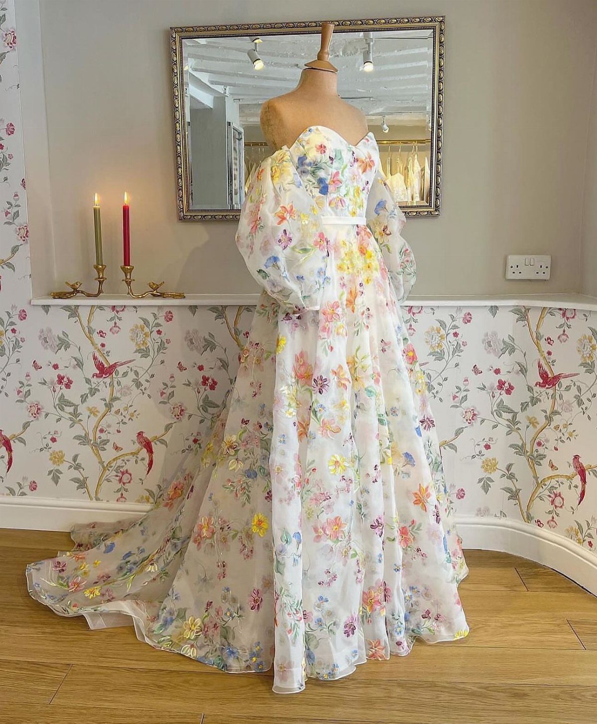 8 Alternative Wedding Dresses for Every Kind of Modern Bride 5 A white wedding gown with colorful floral patterns and large puffed sleeves on a mannequin.