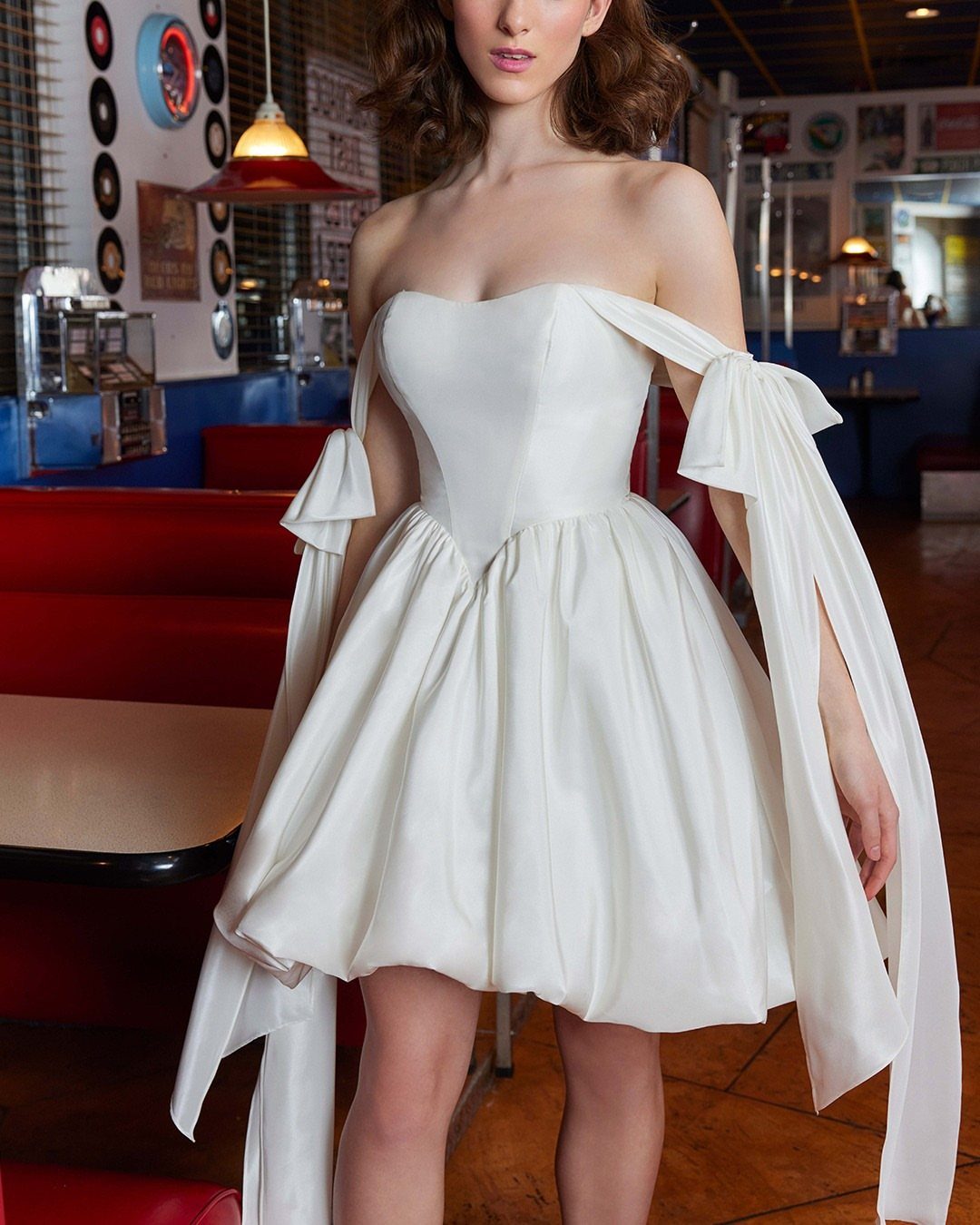 8 Alternative Wedding Dresses for Every Kind of Modern Bride 2 Woman wearing a short, strapless white satin wedding dress with voluminous skirt and long flowing ribbons.
