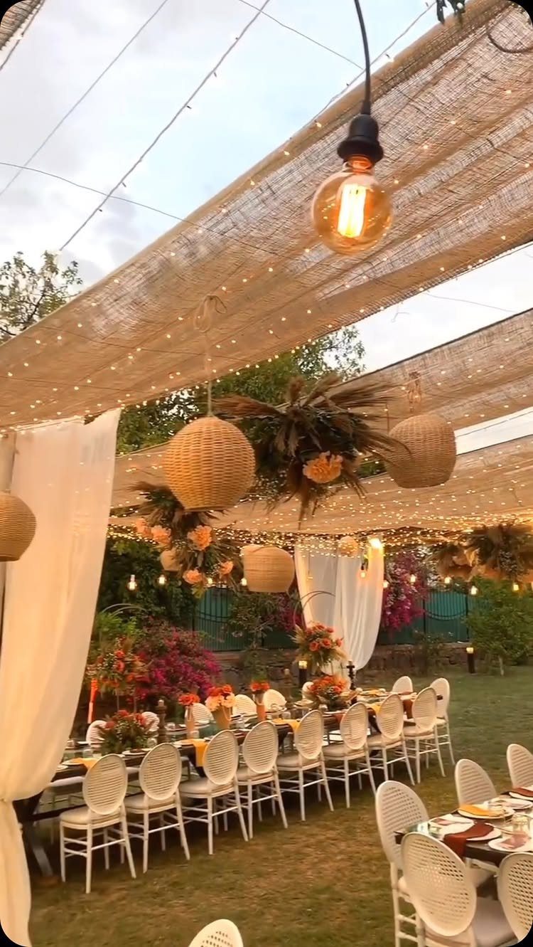 15 Boho Wedding Flowers and Ideas for the Free-Spirited Bride 5 Outdoor wedding reception with burlap canopy, string lights, hanging lanterns, and dining tables on a lawn.