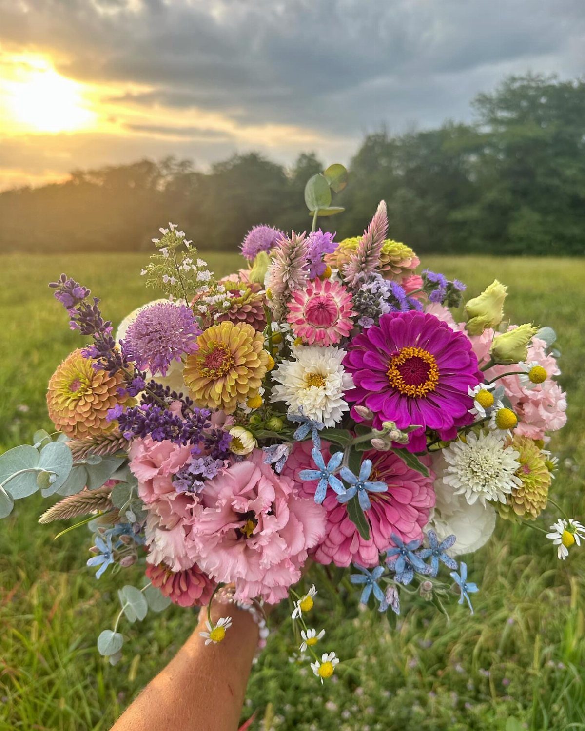 15 Boho Wedding Flowers and Ideas for the Free-Spirited Bride 2 A colorful wildflower bouquet with pink and purple blooms held in a field at sunset.