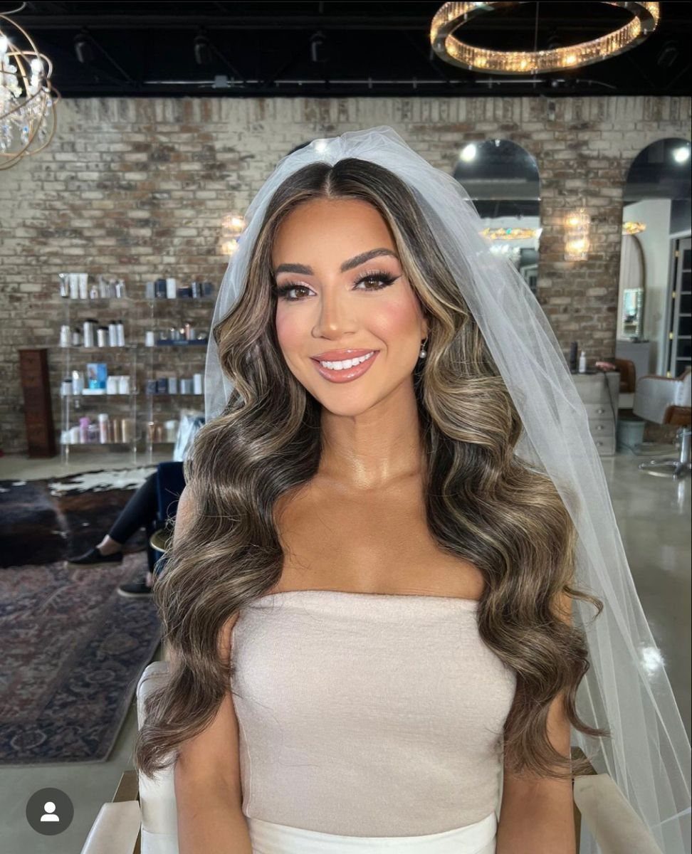 8 Bridal Hair with Veil Ideas for Every Length and Style 5 A woman with long wavy brown hair and a white veil smiling in a salon.