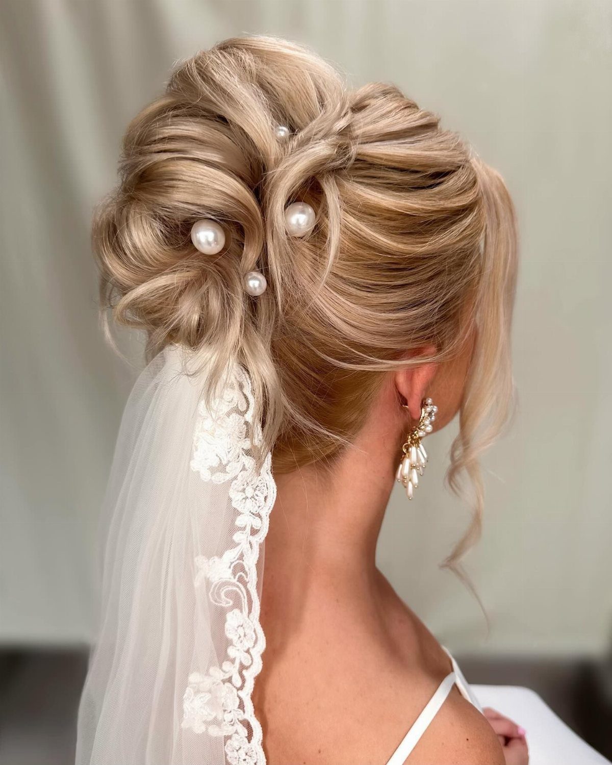 8 Bridal Hair with Veil Ideas for Every Length and Style 6 Blonde hair styled in a textured updo with large pearls and a lace-edged wedding veil.