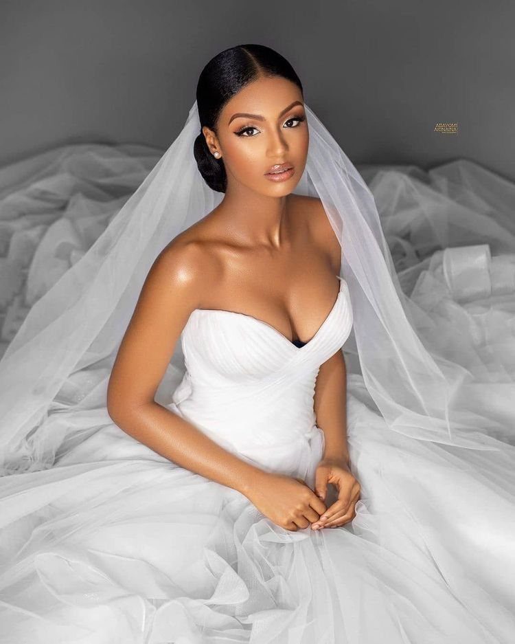 8 Bridal Hair with Veil Ideas for Every Length and Style 7 A woman in a white wedding dress and sheer veil sitting among white tulle fabric.