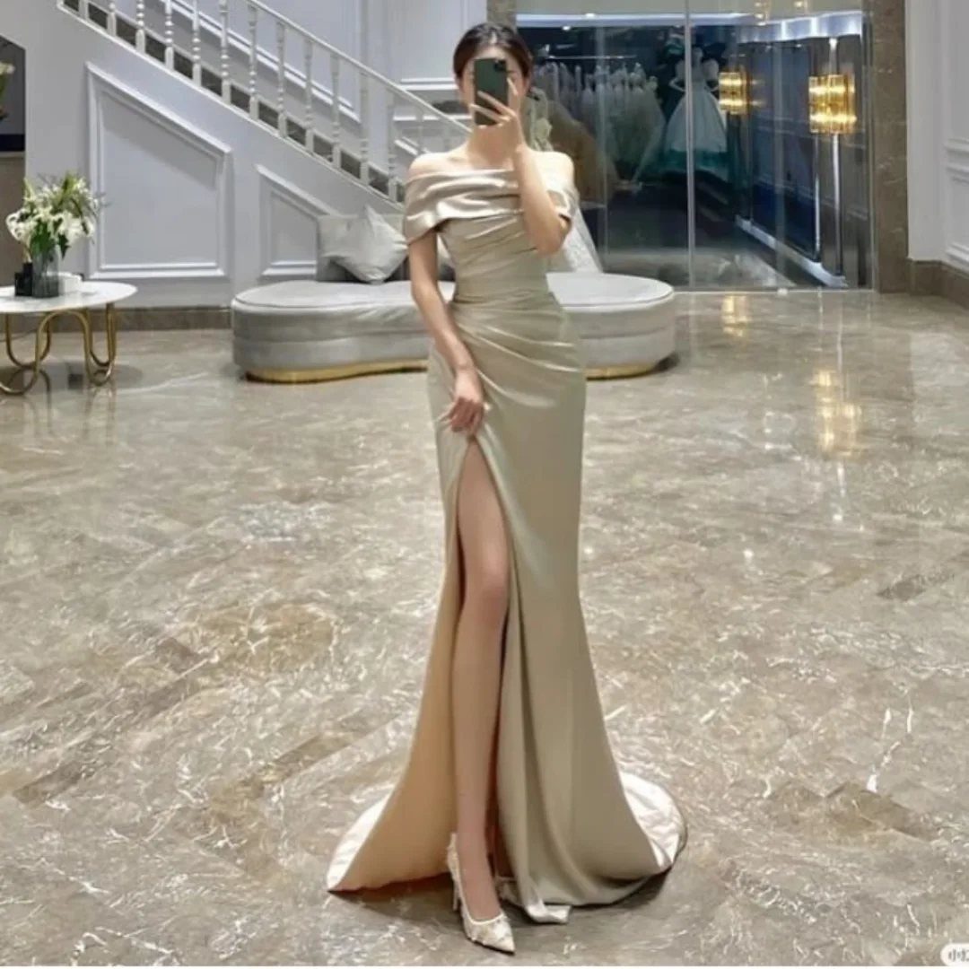 A woman wearing a champagne satin floor-length gown with a high leg slit.