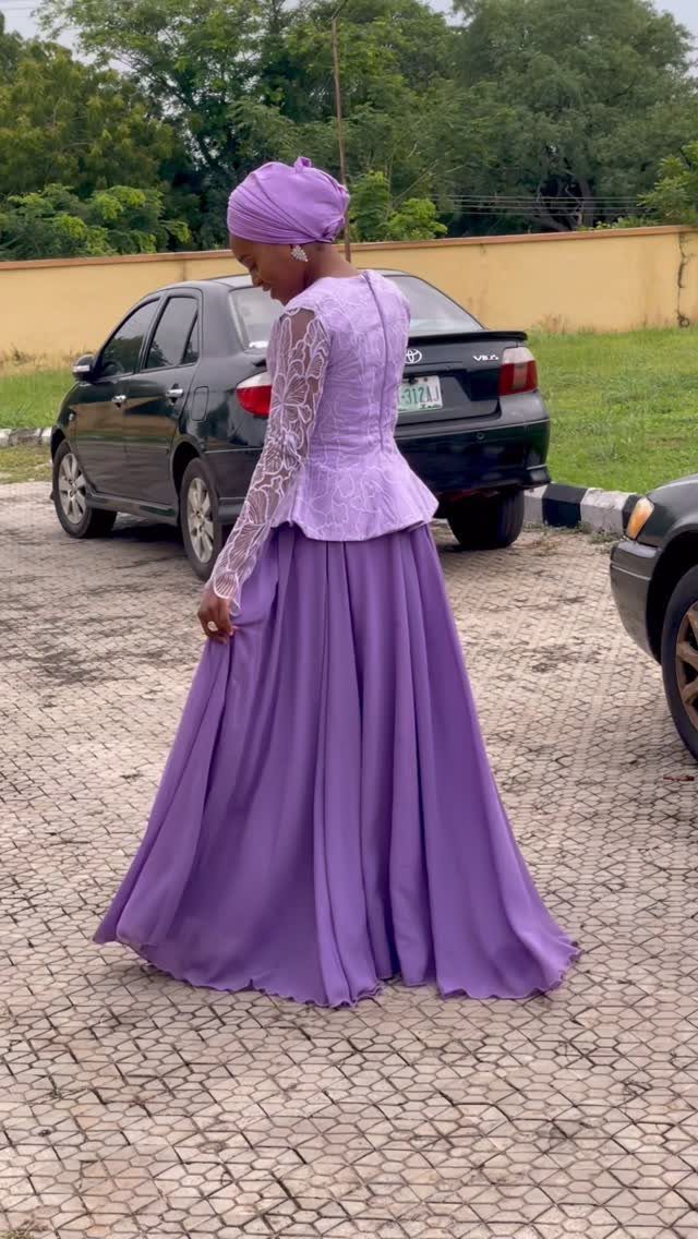 A woman in a long lavender dress with lace sleeves and a matching headwrap.