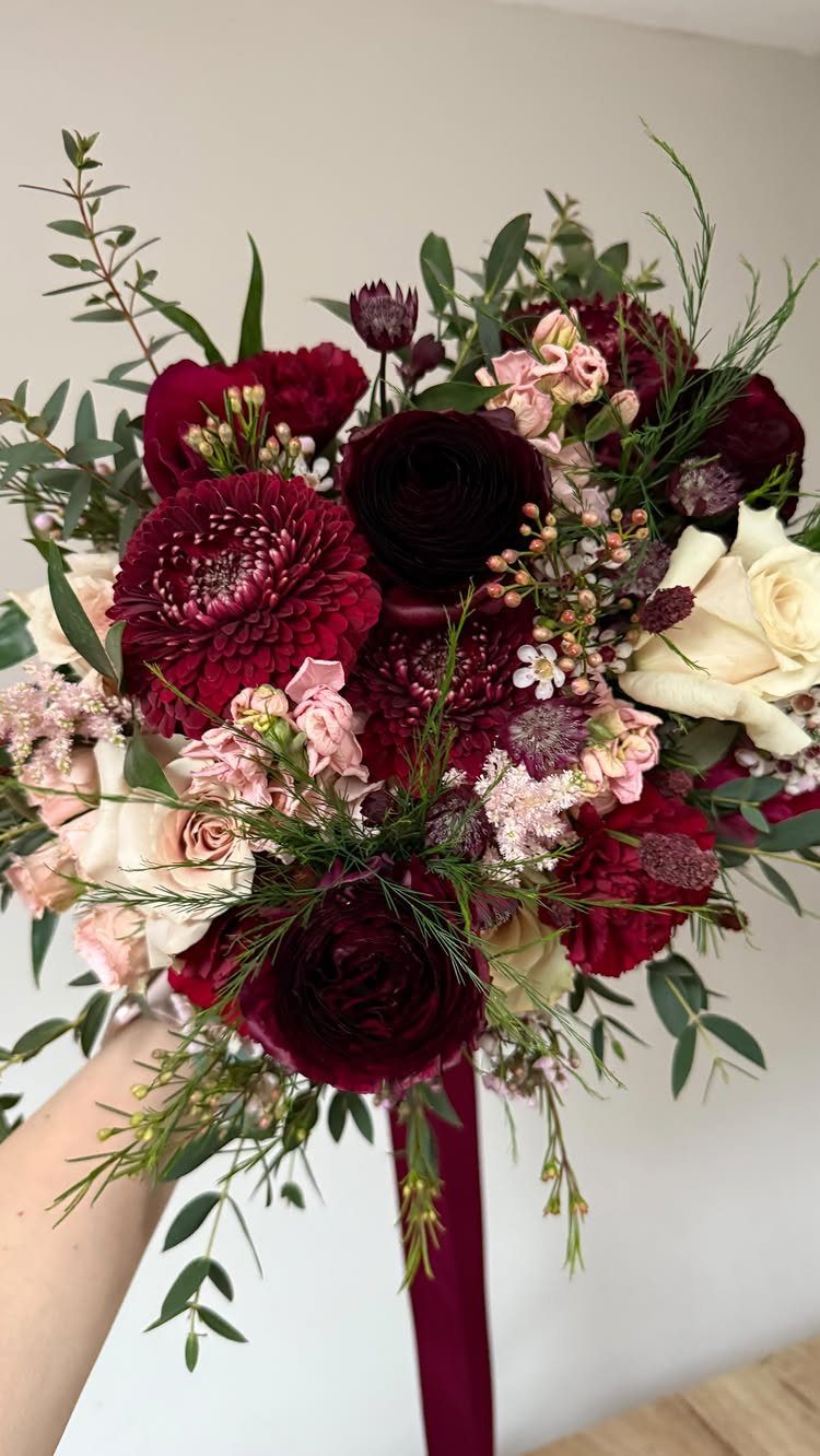 10 Burgundy and Blush Wedding Ideas for Color, Flowers & Decor 6 A large bouquet of burgundy dahlias, dark roses, and blush pink flowers with green foliage.