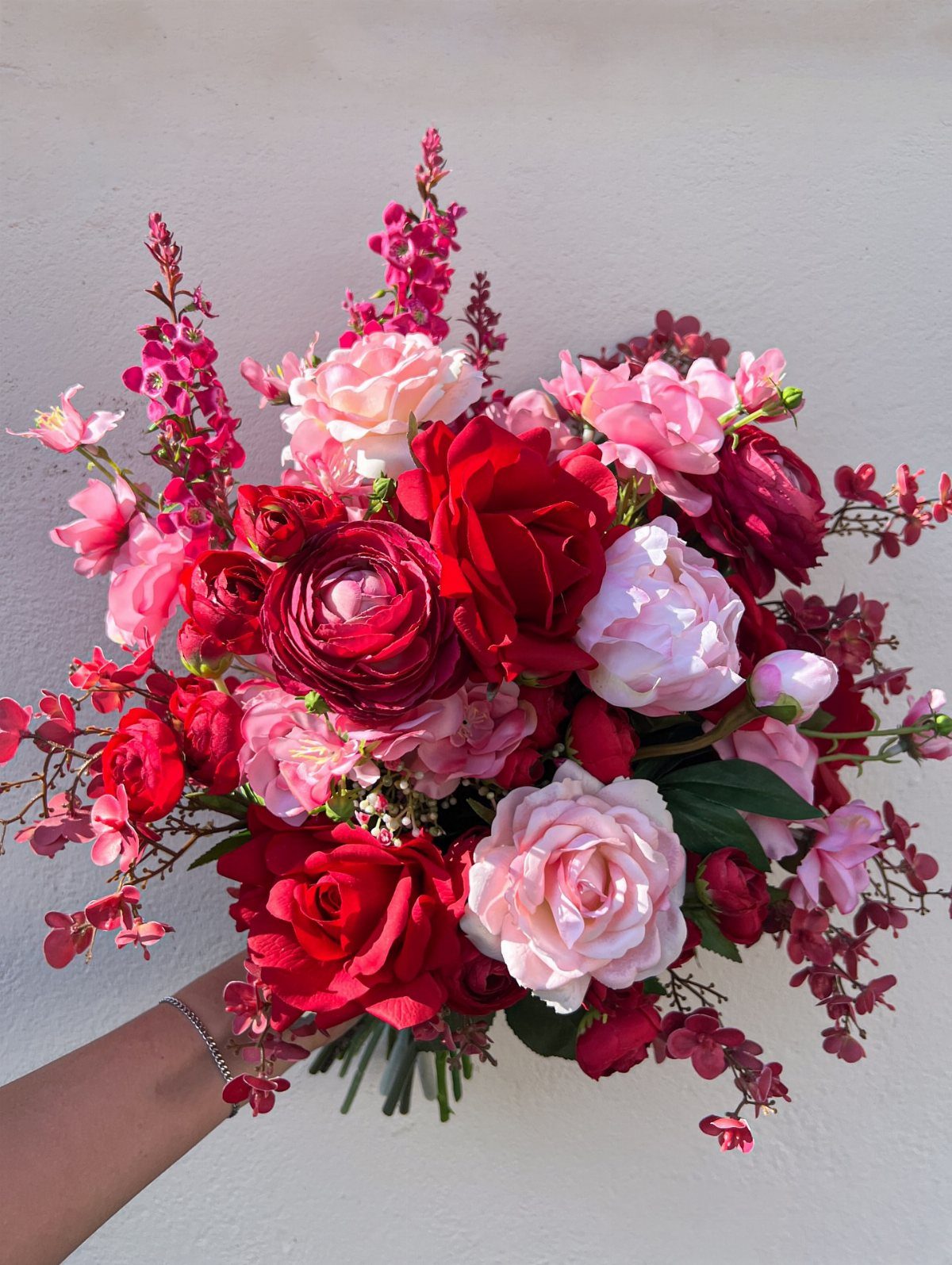 10 Burgundy and Blush Wedding Ideas for Color, Flowers & Decor 3 A hand holding a bouquet of burgundy and blush roses with various pink flowers.