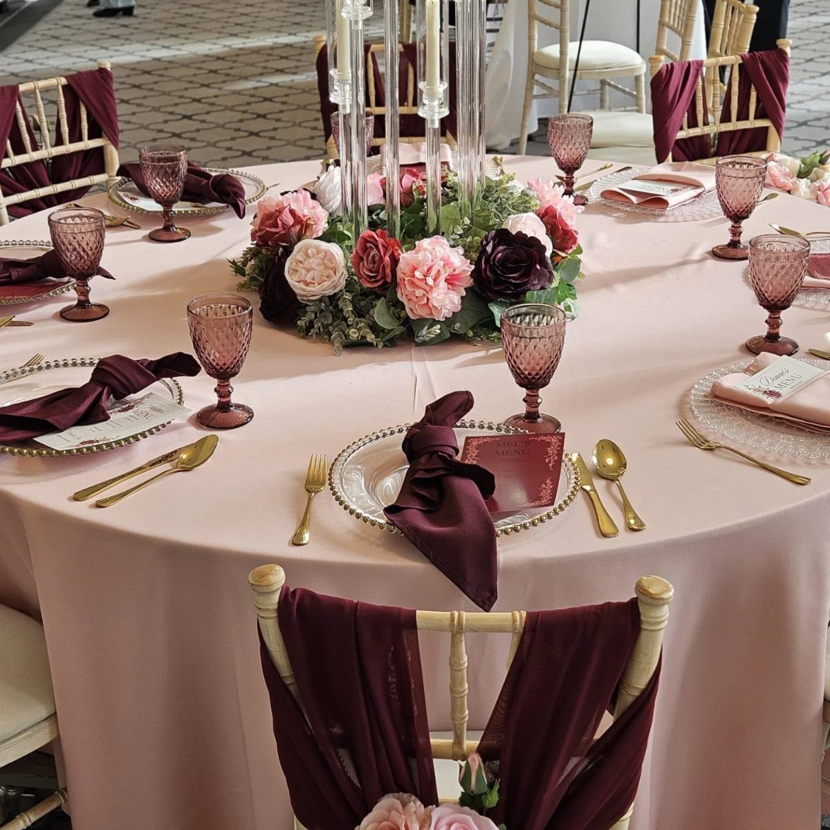 10 Burgundy and Blush Wedding Ideas for Color, Flowers & Decor 2 A round table set with blush linens, burgundy napkins, gold cutlery, and a rose centerpiece.