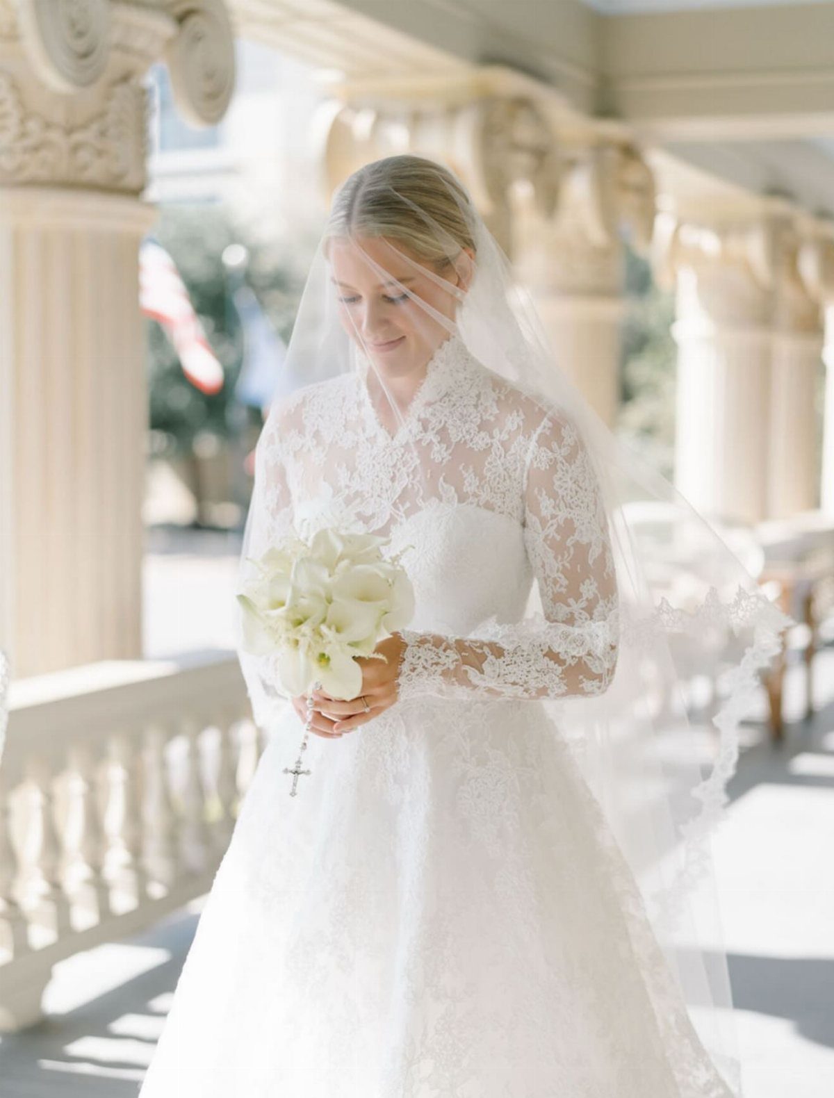 Catholic Wedding Dresses for Modest Church Ceremonies: 6 Ideas 6 A bride in a long-sleeved lace wedding dress and veil holding white calla lilies.