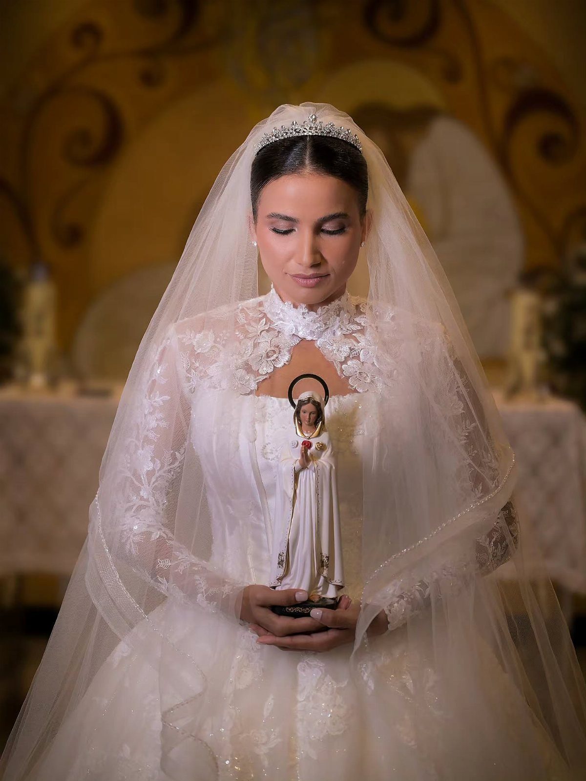 Catholic Wedding Dresses for Modest Church Ceremonies: 6 Ideas 4 A bride in a long-sleeved lace wedding gown holding a small religious figurine.