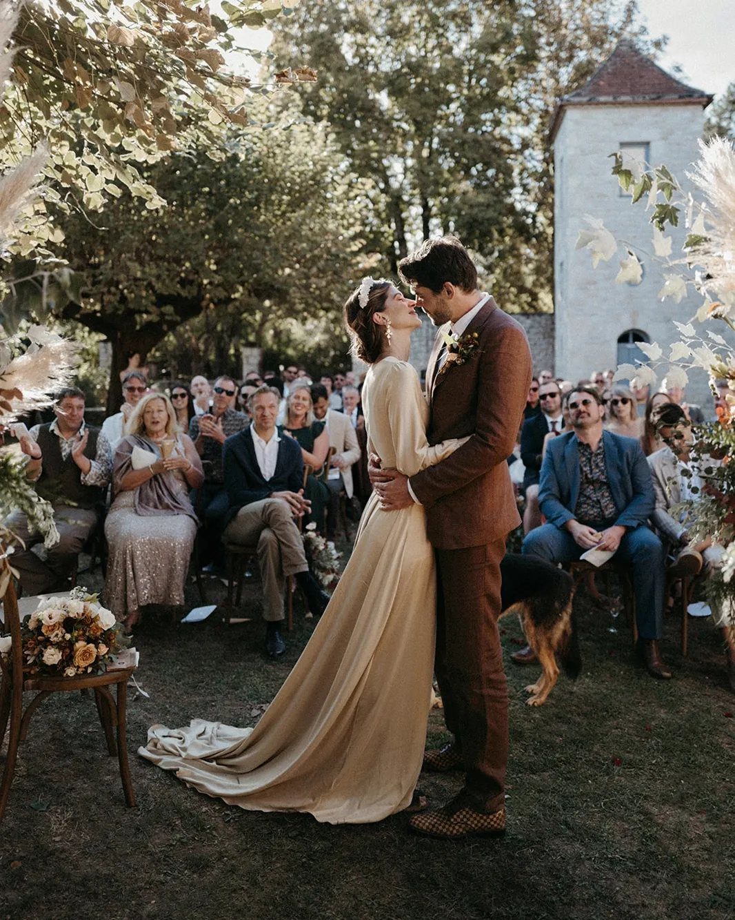 9 Champagne and Green Wedding Ideas for Every Detail 5 A bride in a champagne gown and a groom embrace during an outdoor wedding ceremony.