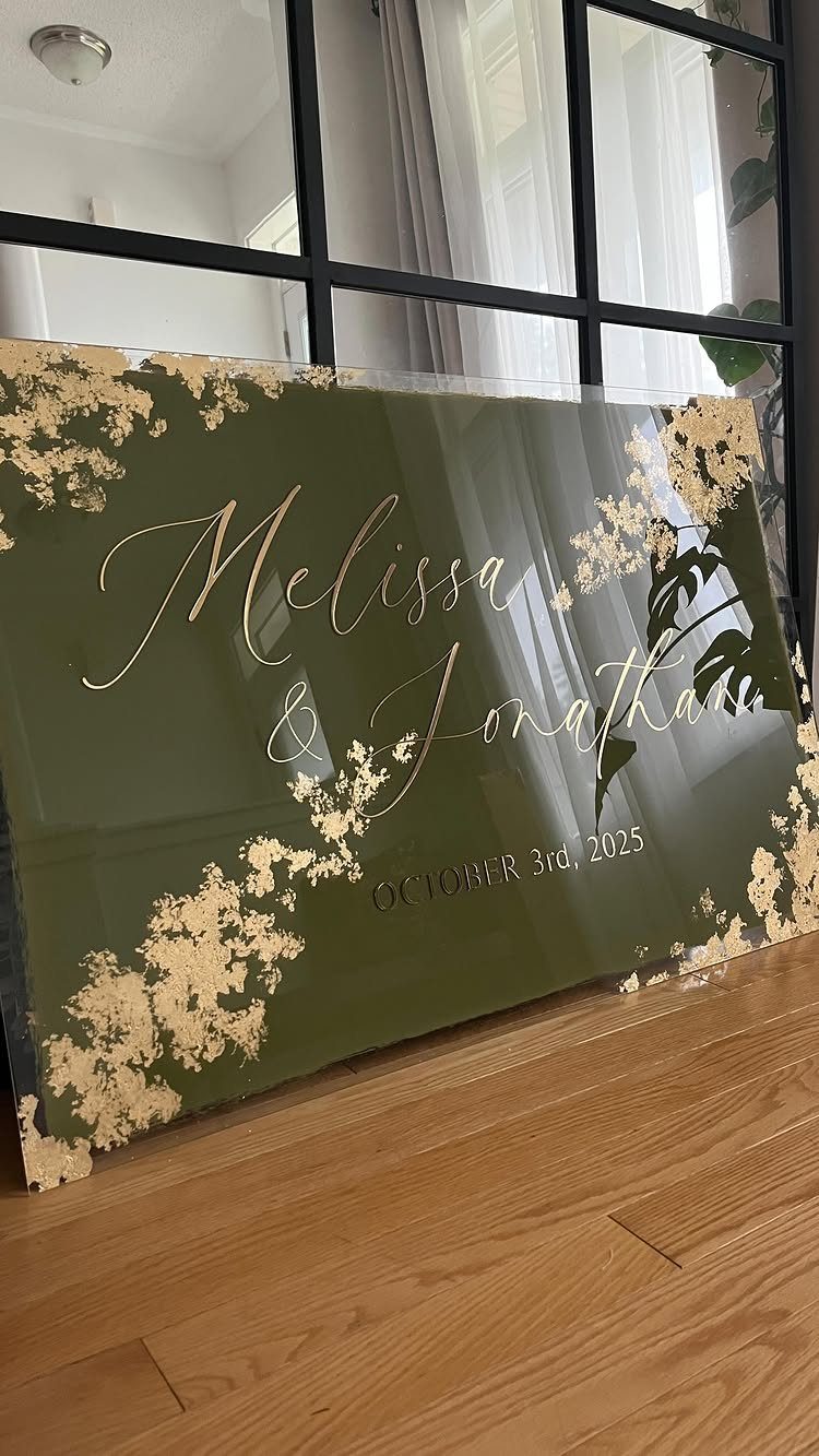 9 Champagne and Green Wedding Ideas for Every Detail 9 A dark green acrylic wedding sign with gold floral accents and names written in gold script.