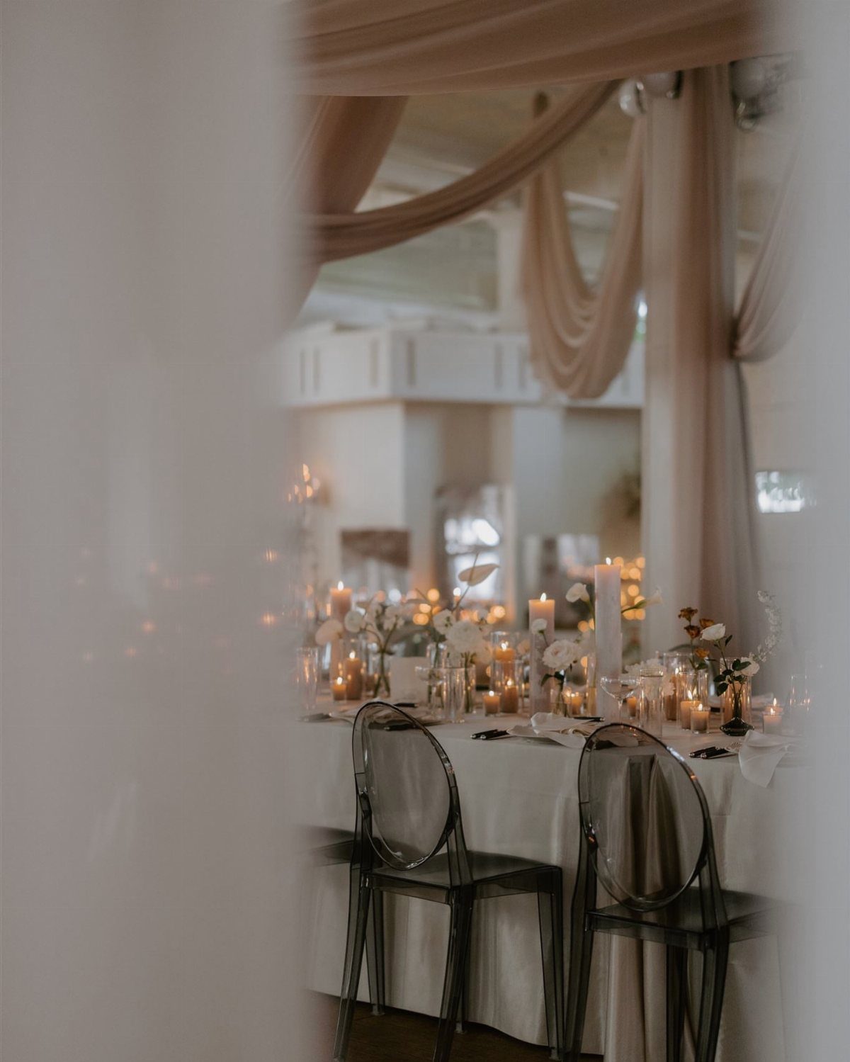9 Champagne and Green Wedding Ideas for Every Detail 2 A wedding reception table featuring champagne linens, white flowers, and glowing candles in a draped room.