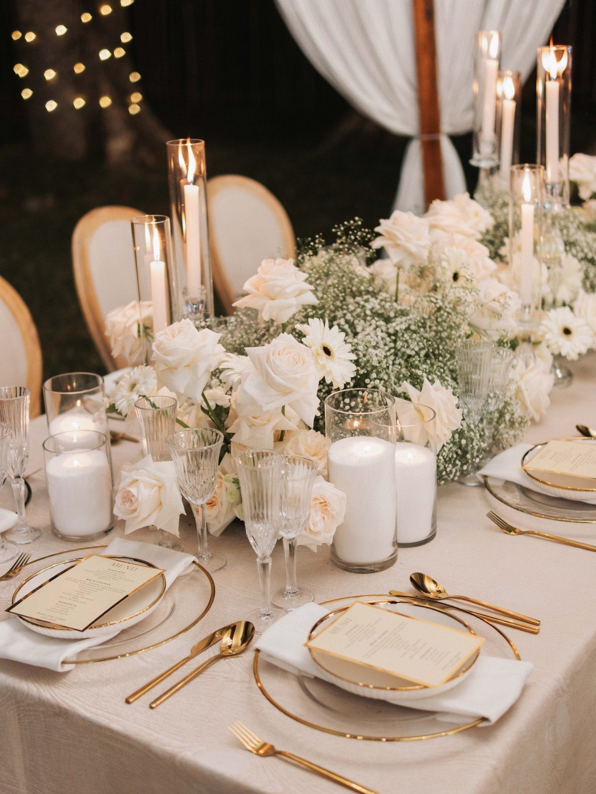 9 Champagne and Green Wedding Ideas for Every Detail 7 Champagne colored wedding table setting with white roses, greenery, gold cutlery, and glowing candles.