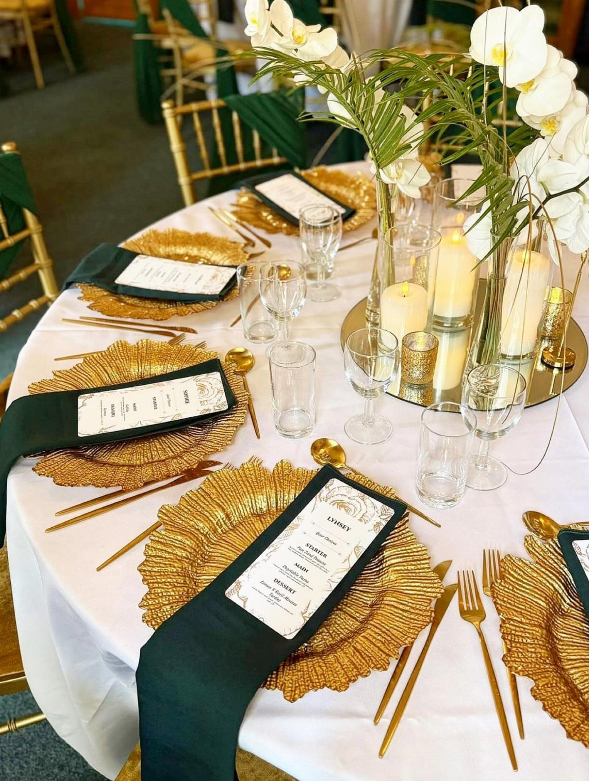 9 Champagne and Green Wedding Ideas for Every Detail 4 Gold charger plates and cutlery arranged on a white wedding table with green napkins and white orchids.