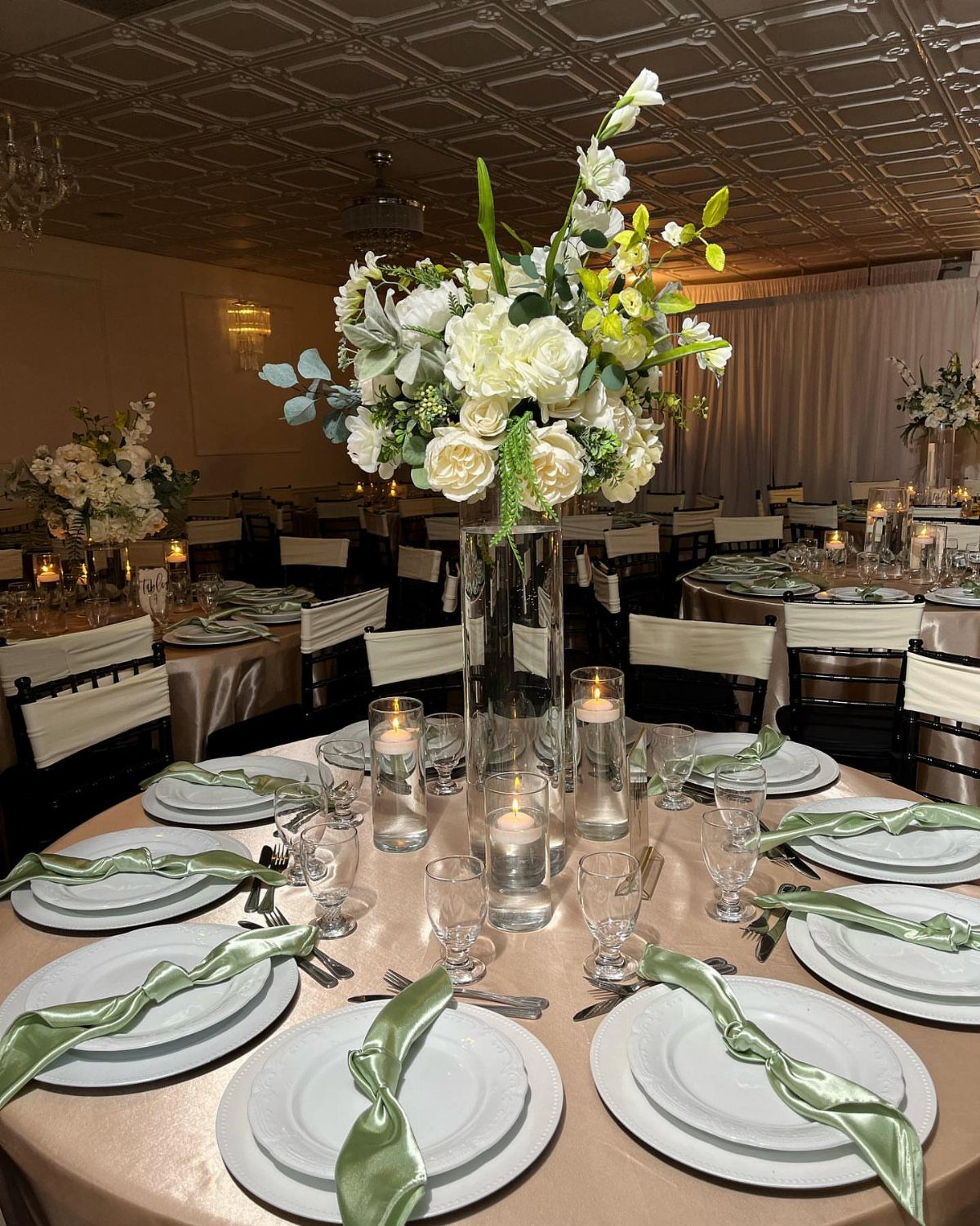 9 Champagne and Green Wedding Ideas for Every Detail 1 A tall glass vase filled with white roses and sage green eucalyptus greenery on a wedding table.
