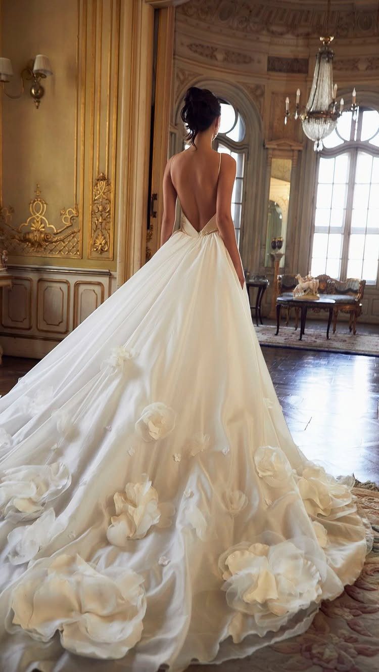 Woman in a white wedding dress with a long floral train in an ornate room.
