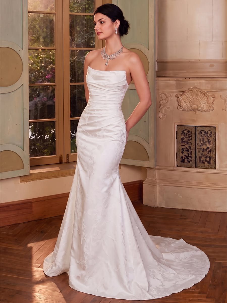 Woman wearing a white strapless mermaid wedding dress with a subtle train standing indoors.