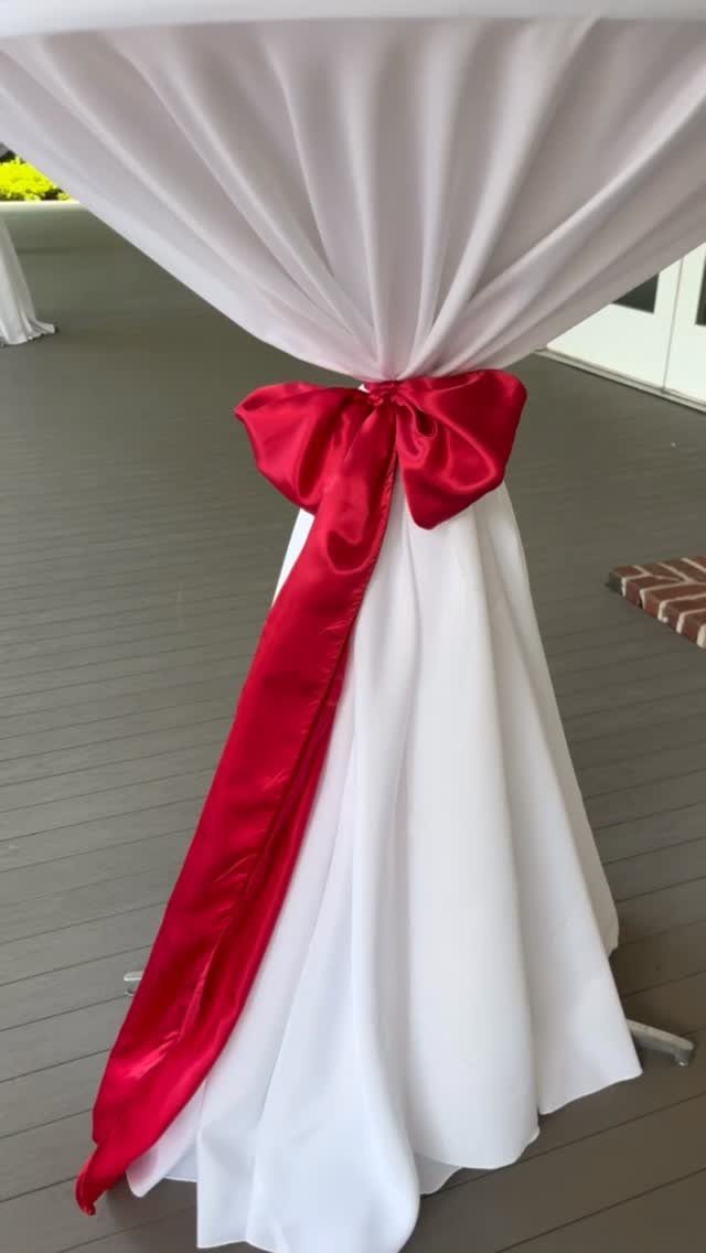 A white draped cocktail table cinched with a large red satin bow on a deck.
