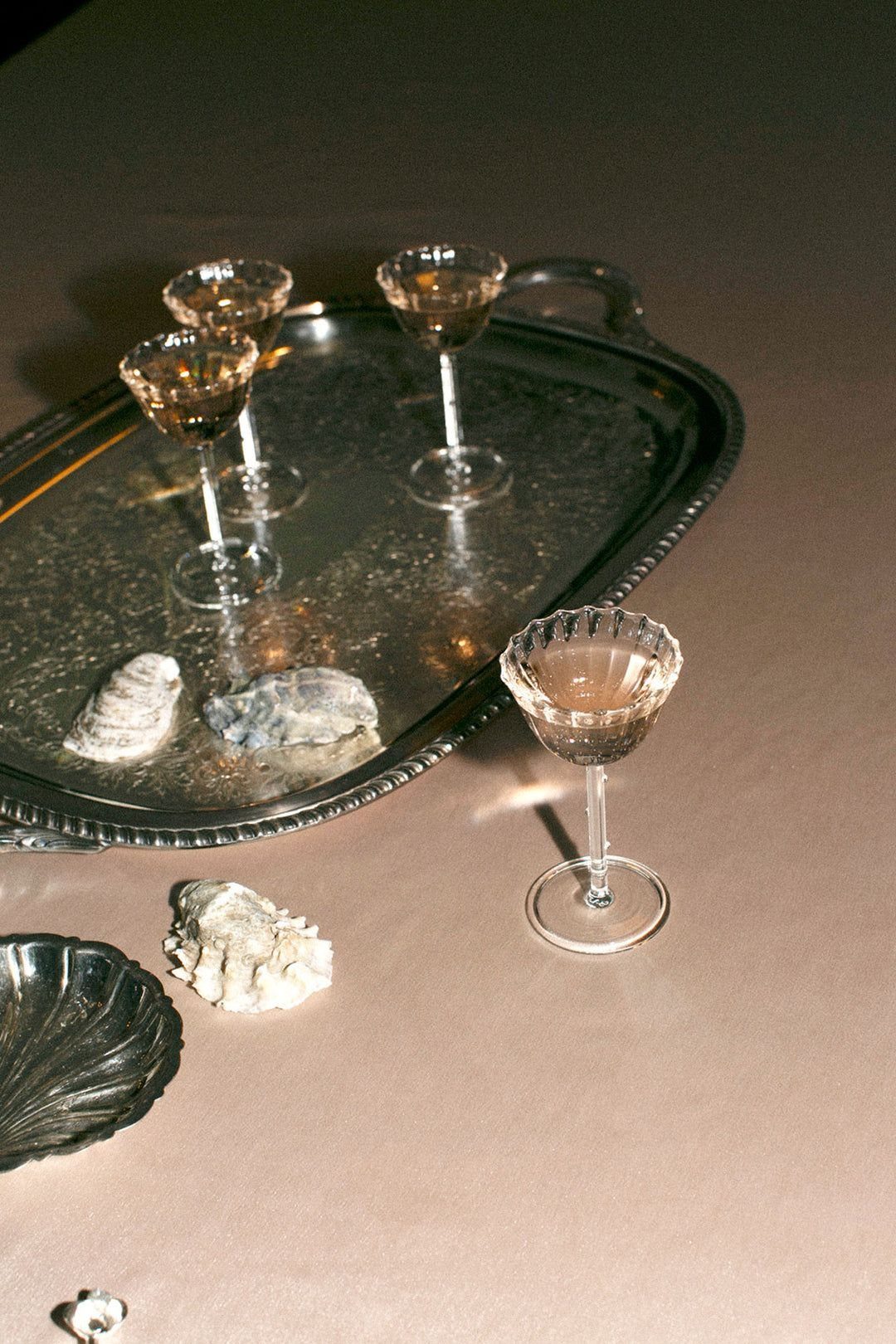 Elegant coupe glasses and oyster shells arranged on a silver tray and beige tablecloth.