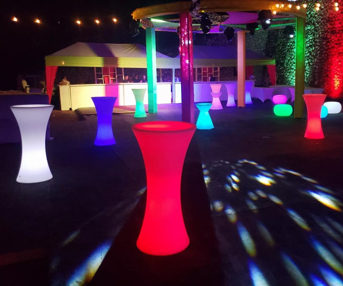 Colorful glowing LED cocktail tables scattered across a dark outdoor event space at night.