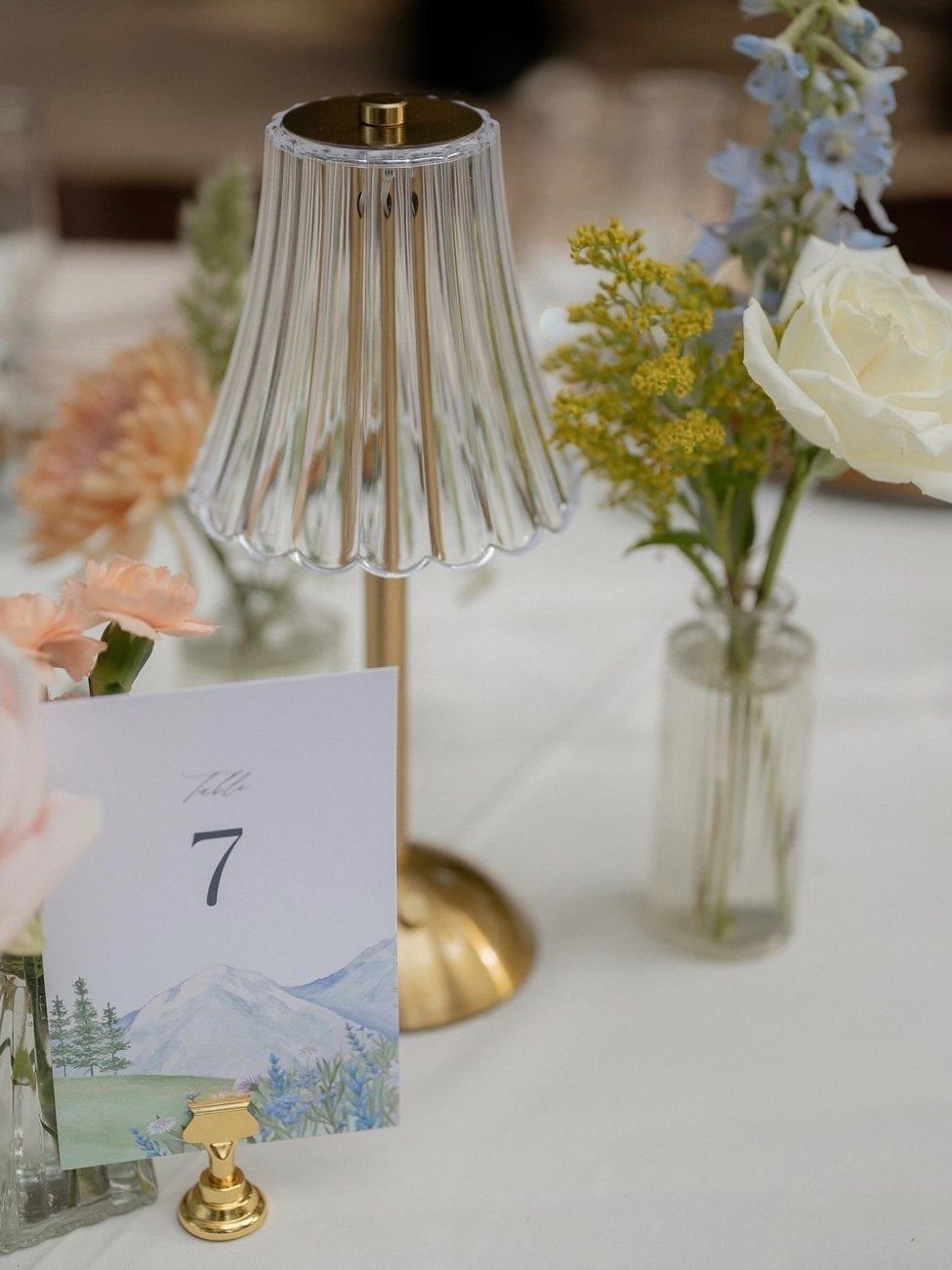 A small gold table lamp with a ribbed glass shade next to floral arrangements and a table number card.