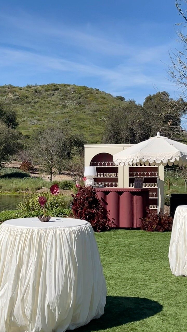 Two cocktail tables covered in pleated white tablecloths on a green lawn outdoors.