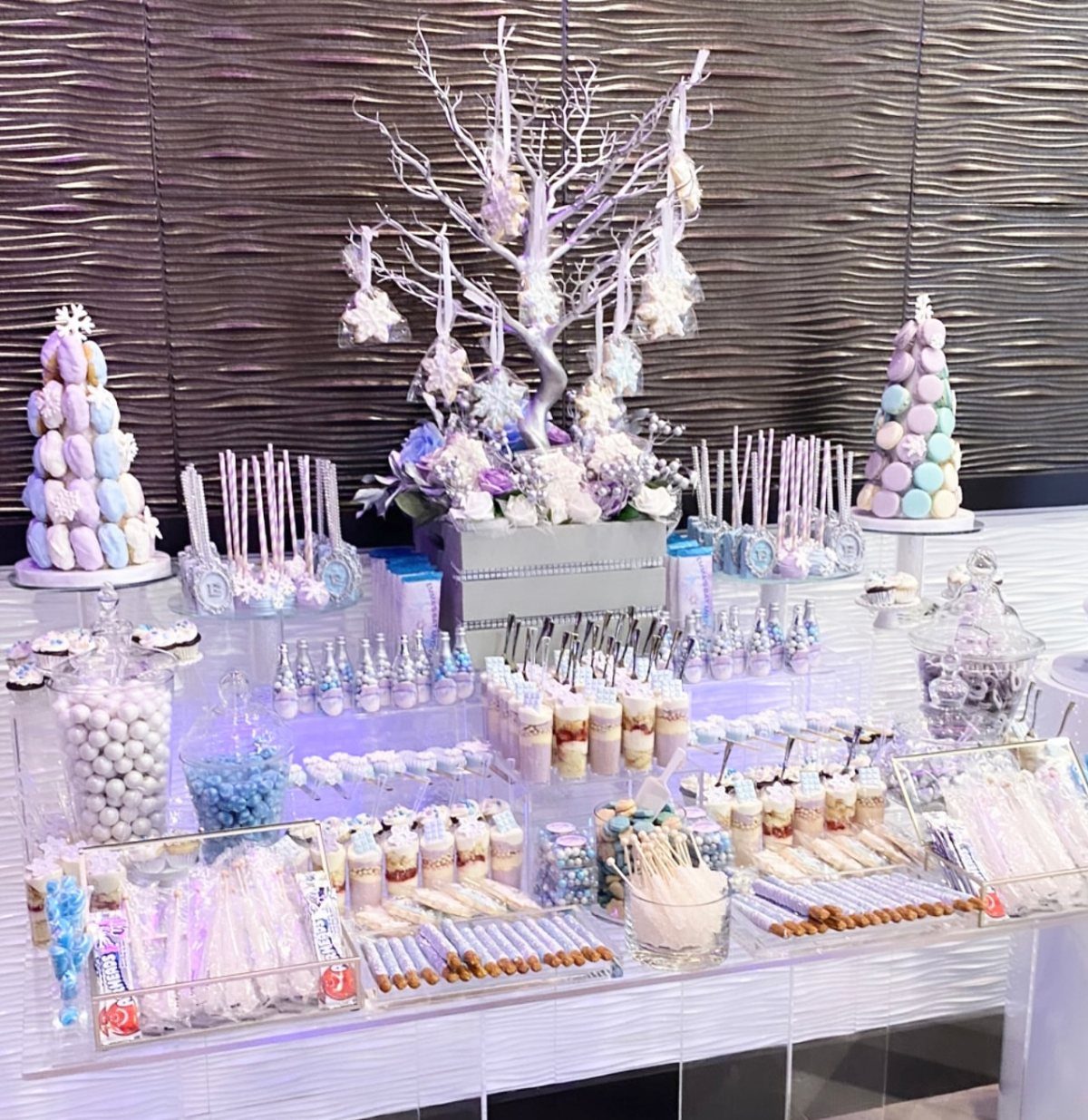 A dessert table display with macaron towers, cake pops, and a white decorative tree centerpiece.