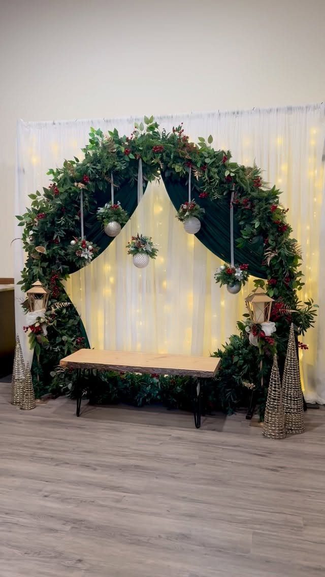 A lush green foliage arch with red berries and hanging ornaments in front of twinkling lights.