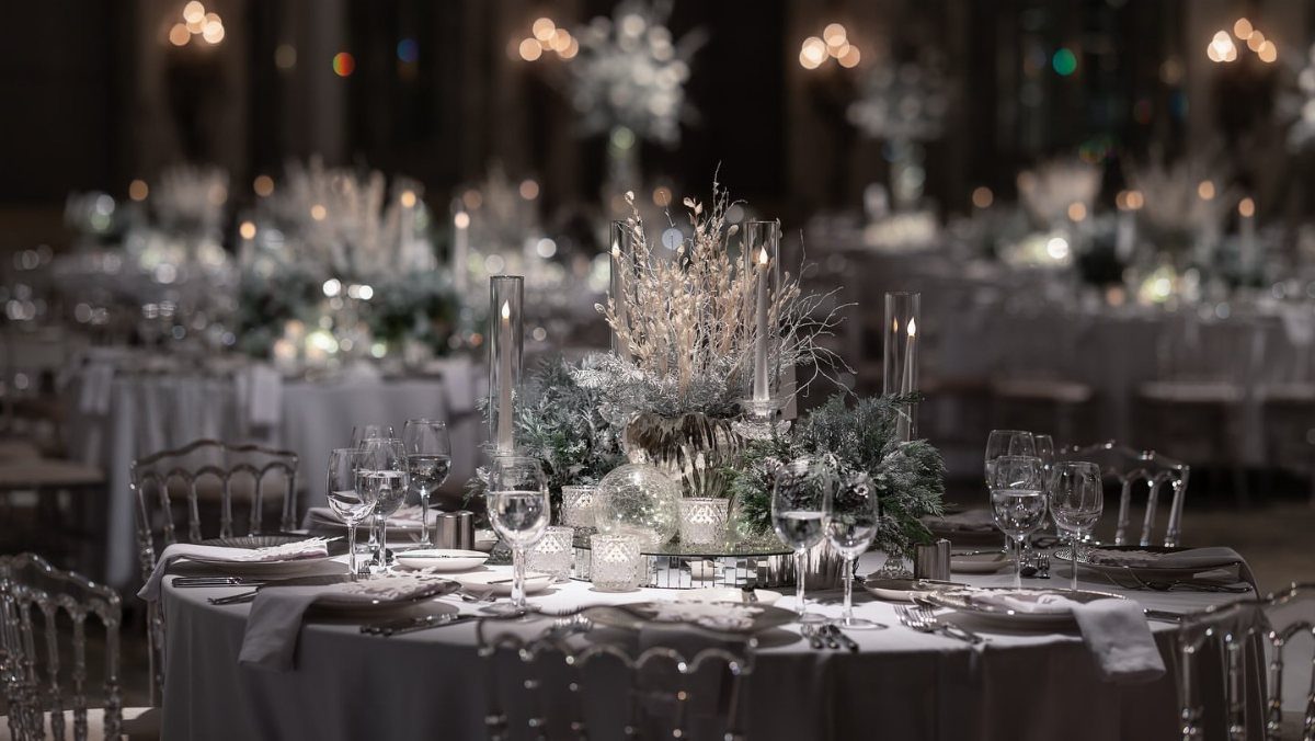 An elegantly set wedding reception table with white linens, crystal glassware, and frosted winter floral centerpieces.