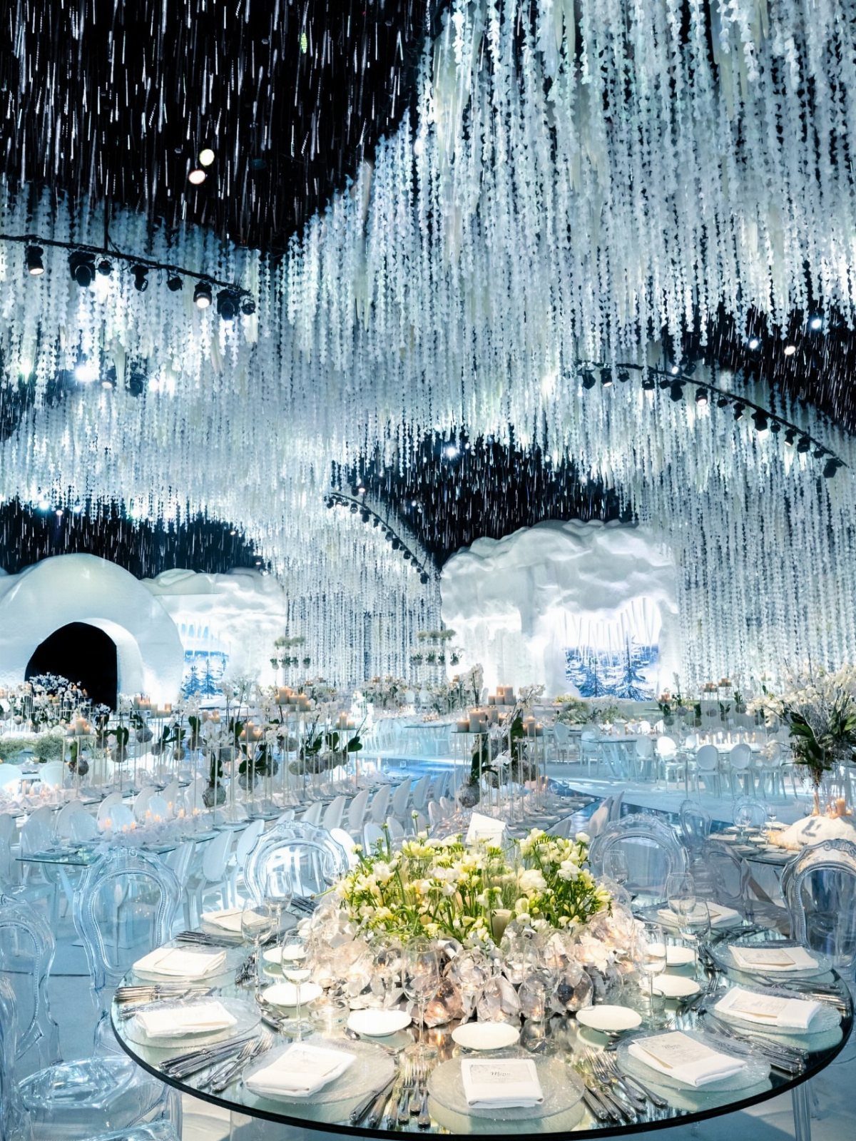Crystal strands hang from a ceiling over a wedding reception with white floral centerpieces.
