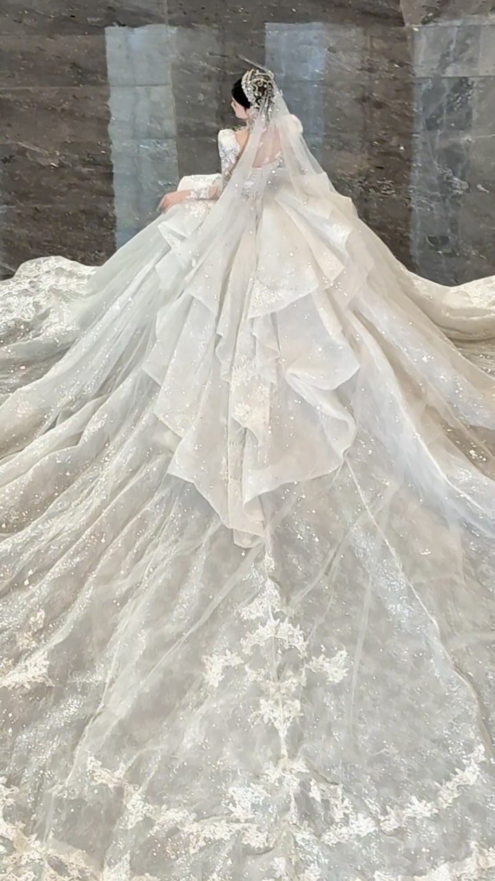A bride in a sparkling white wedding gown with a massive, shimmering lace train.