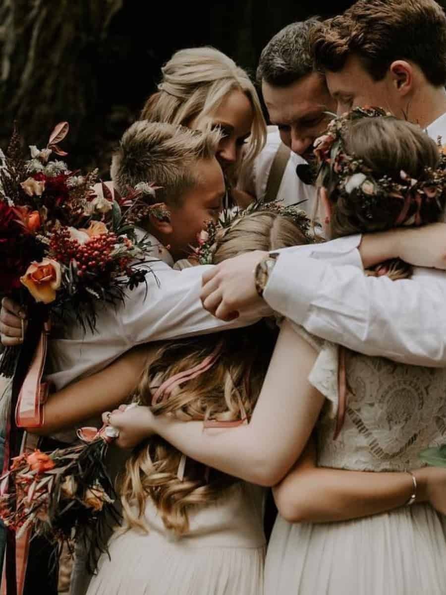 9 Family Wedding Picture Ideas for Every Group 3 A group of family members in wedding attire sharing a warm, close group hug outdoors.