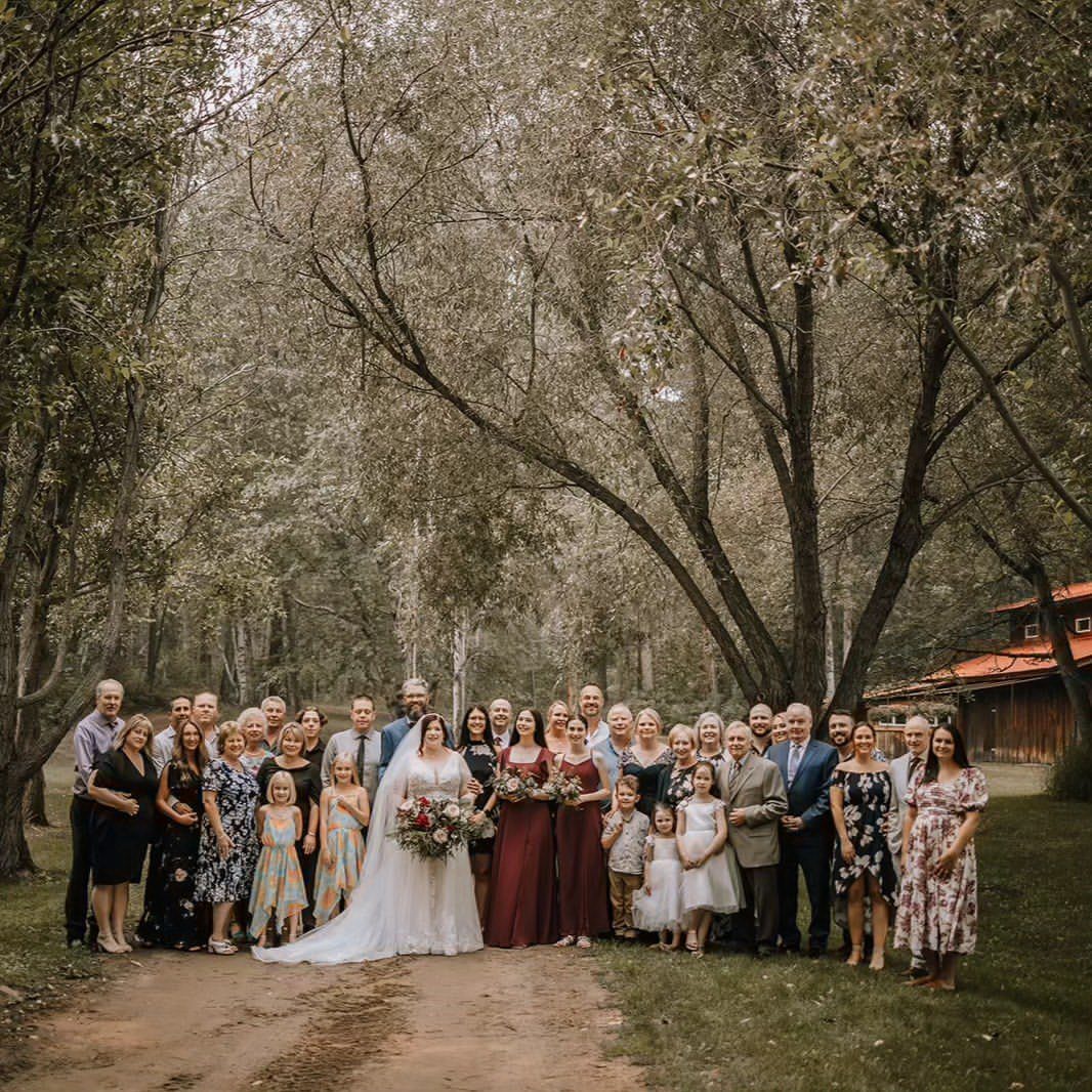 9 Family Wedding Picture Ideas for Every Group 4 A large wedding party posing for a group portrait on a path surrounded by tall trees.