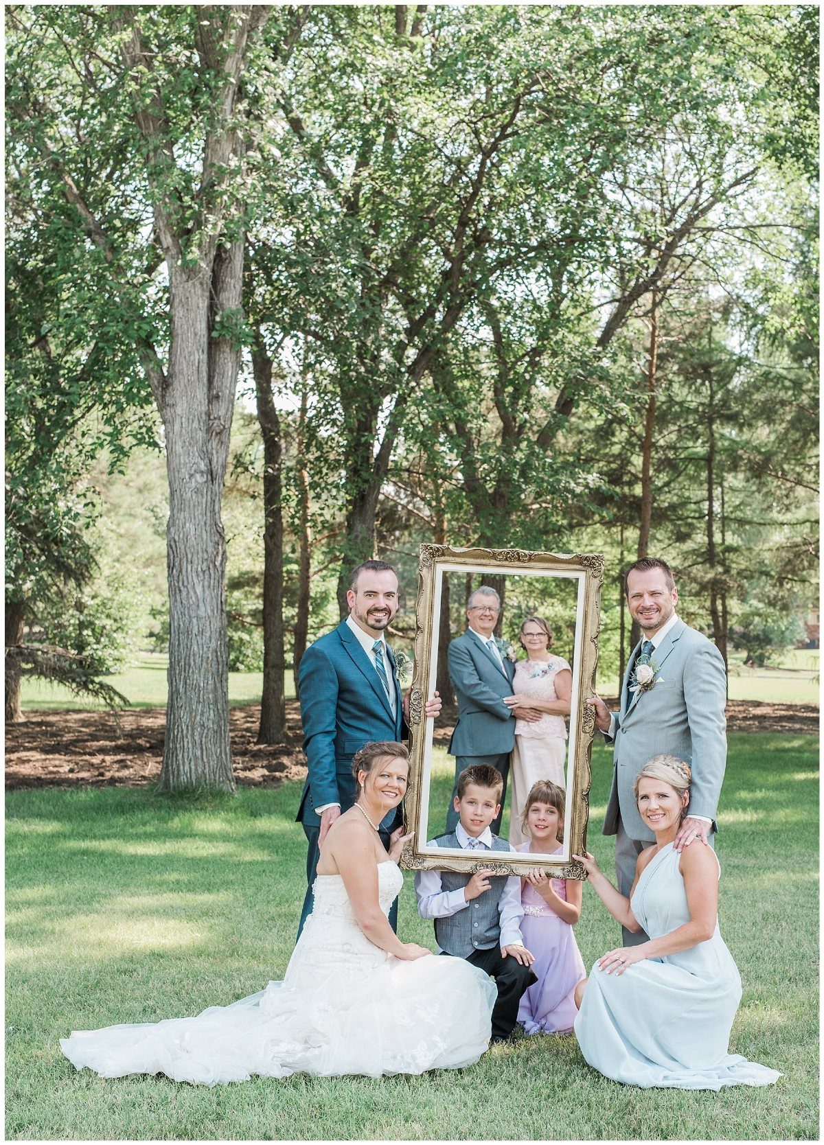 9 Family Wedding Picture Ideas for Every Group 5 A family posing outdoors while holding a large gold frame around several members.
