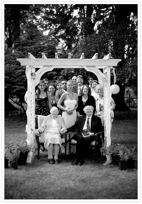 9 Family Wedding Picture Ideas for Every Group 6 A large multi-generational family posing for a portrait under a white wooden pergola outdoors.
