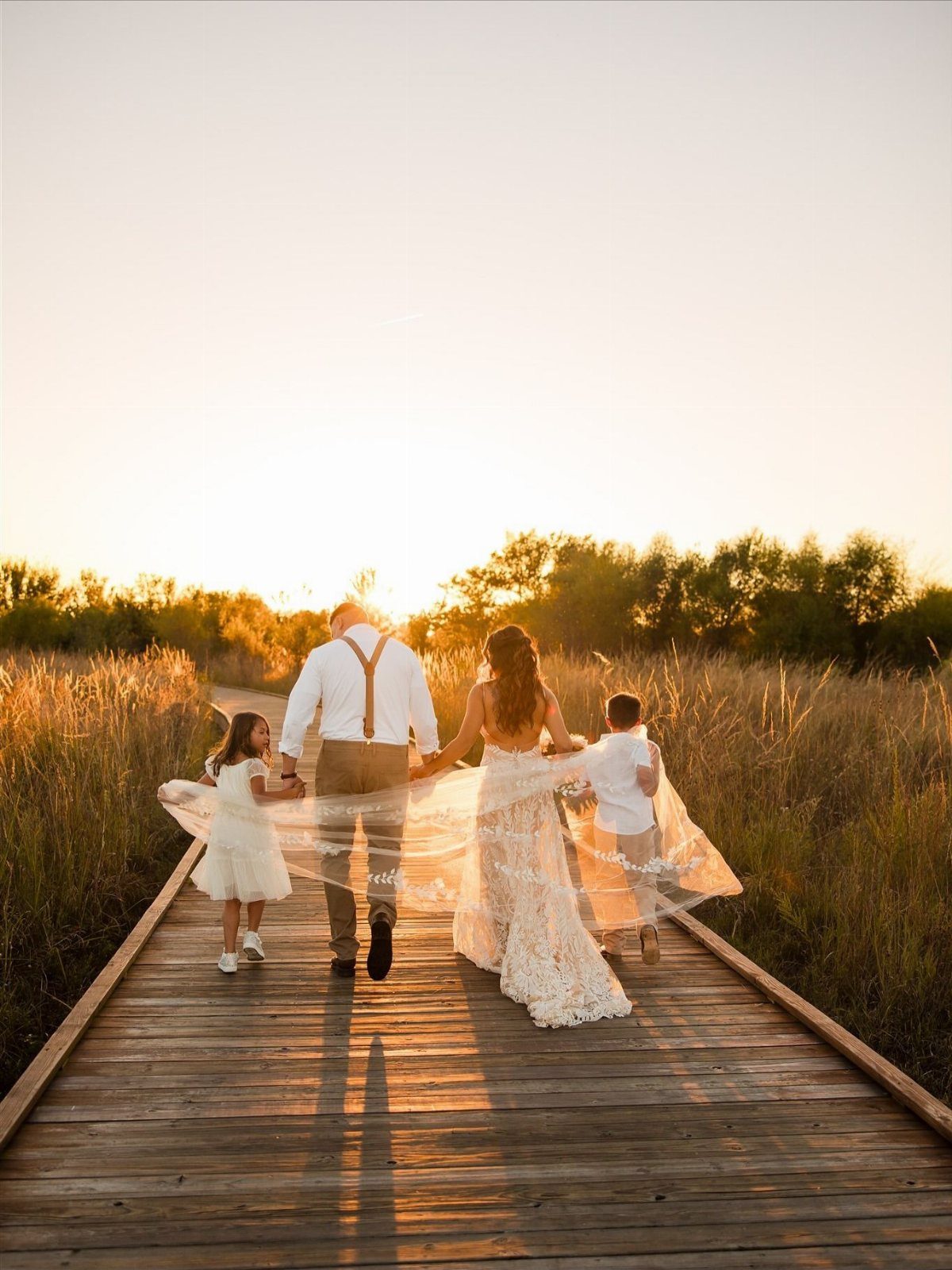 9 Family Wedding Picture Ideas for Every Group 2 A wedding family walking hand-in-hand down a wooden boardwalk during a golden sunset.
