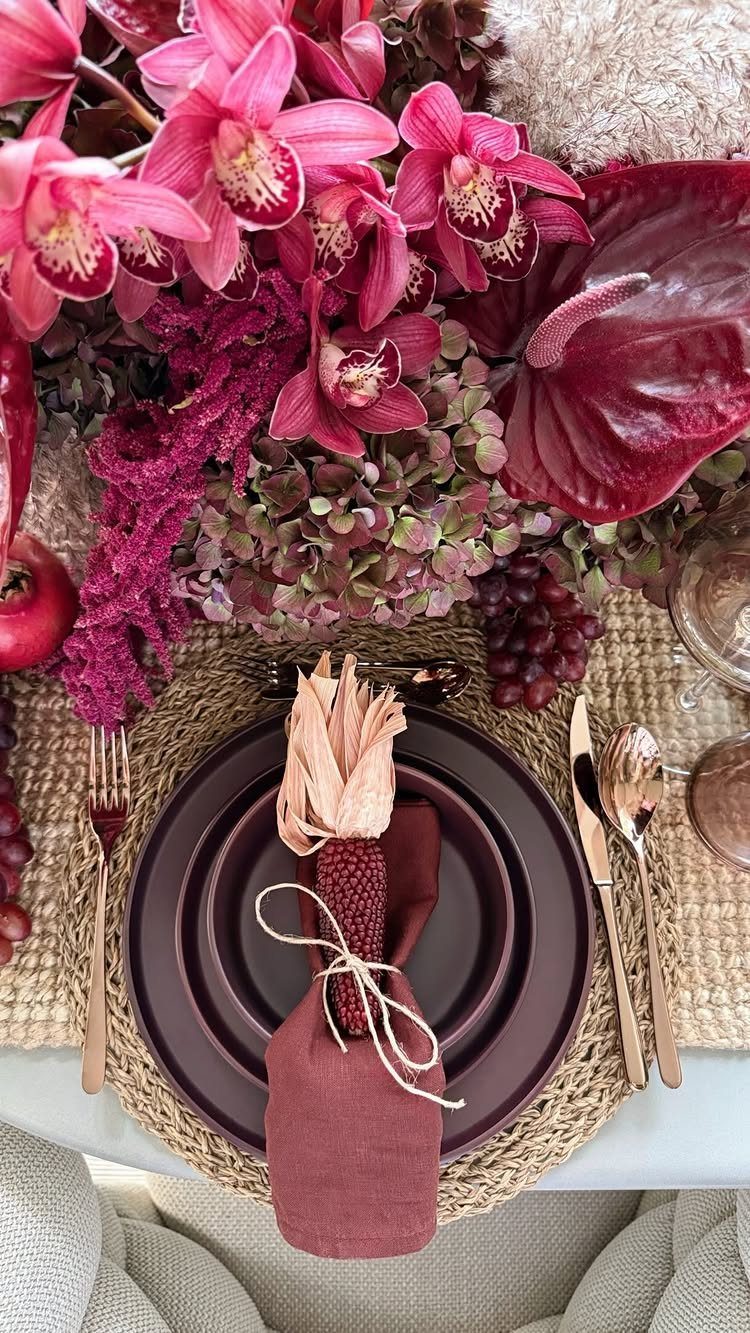 Burgundy plates and napkins set on a woven placemat with dark red floral arrangements.