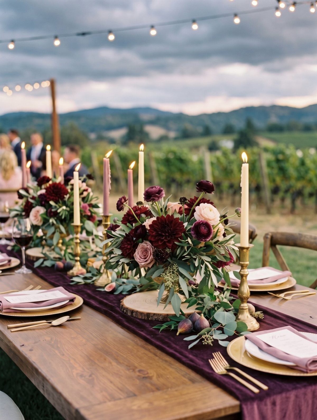 A long wooden table decorated with burgundy velvet runner, gold flatware, and dark floral centerpieces.