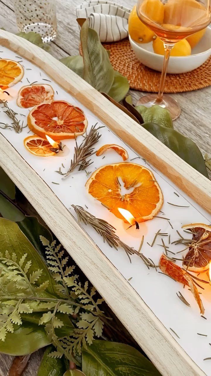 Dried orange slices and rosemary sprigs with lit tea light candles in a white wooden tray.