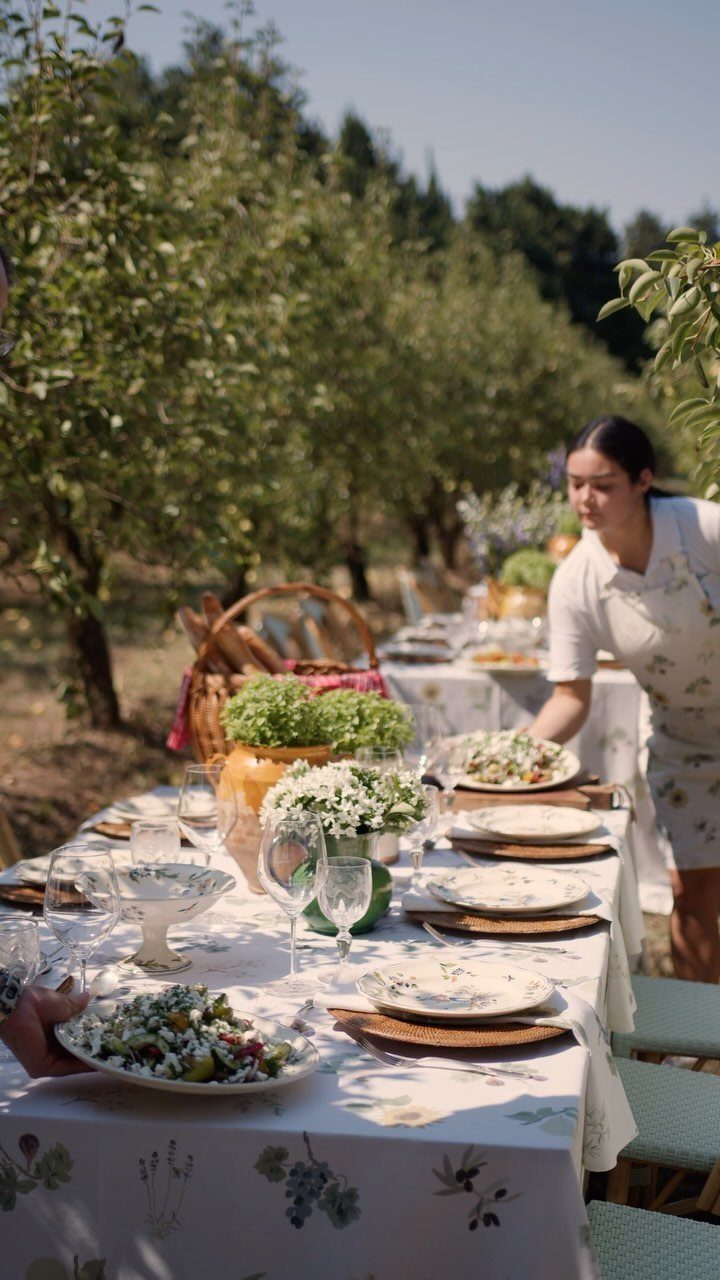 A woman serving a large salad platter at a long outdoor dining table.